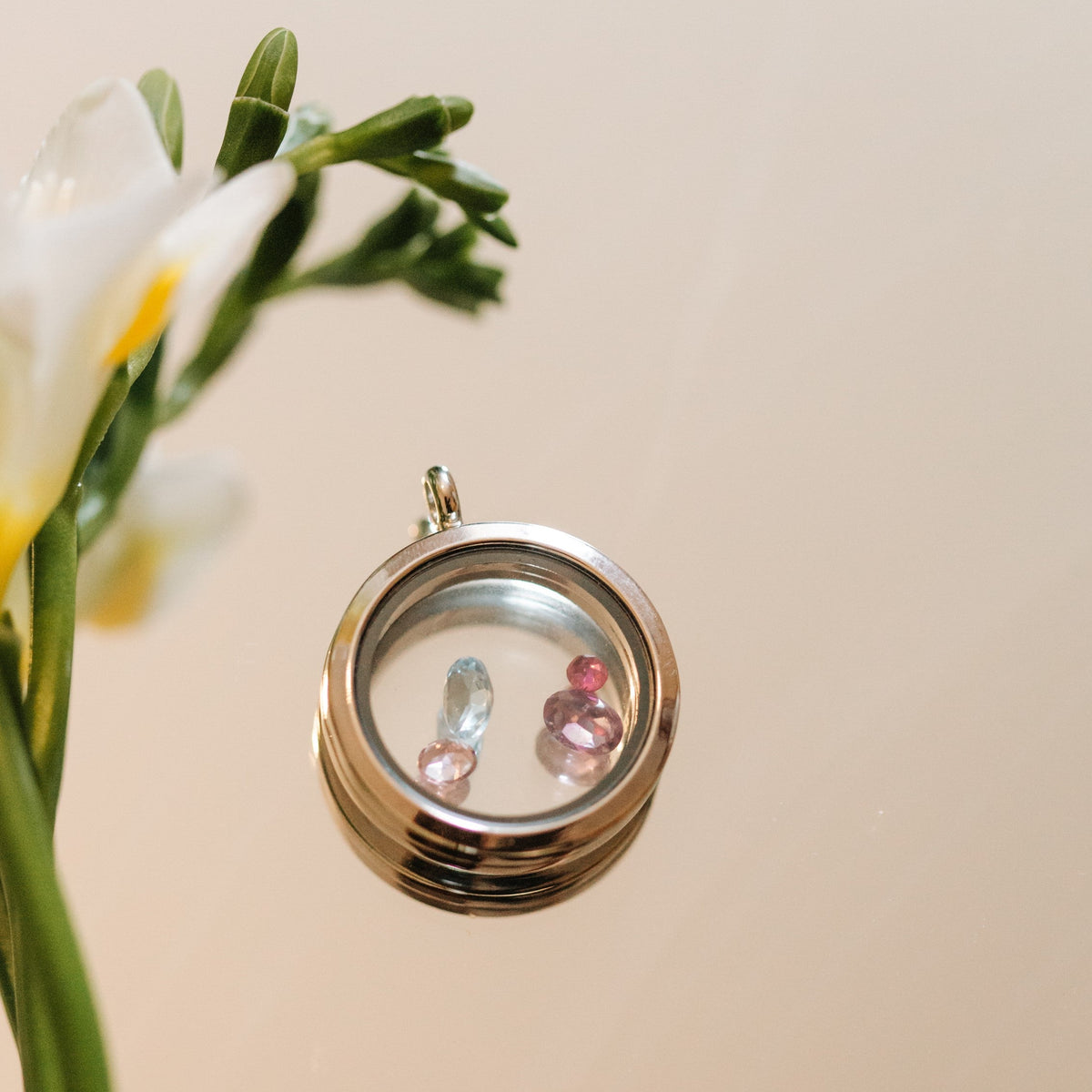 Silver locket with embedded gemstones next to a bouquet of flowers on a beige background
