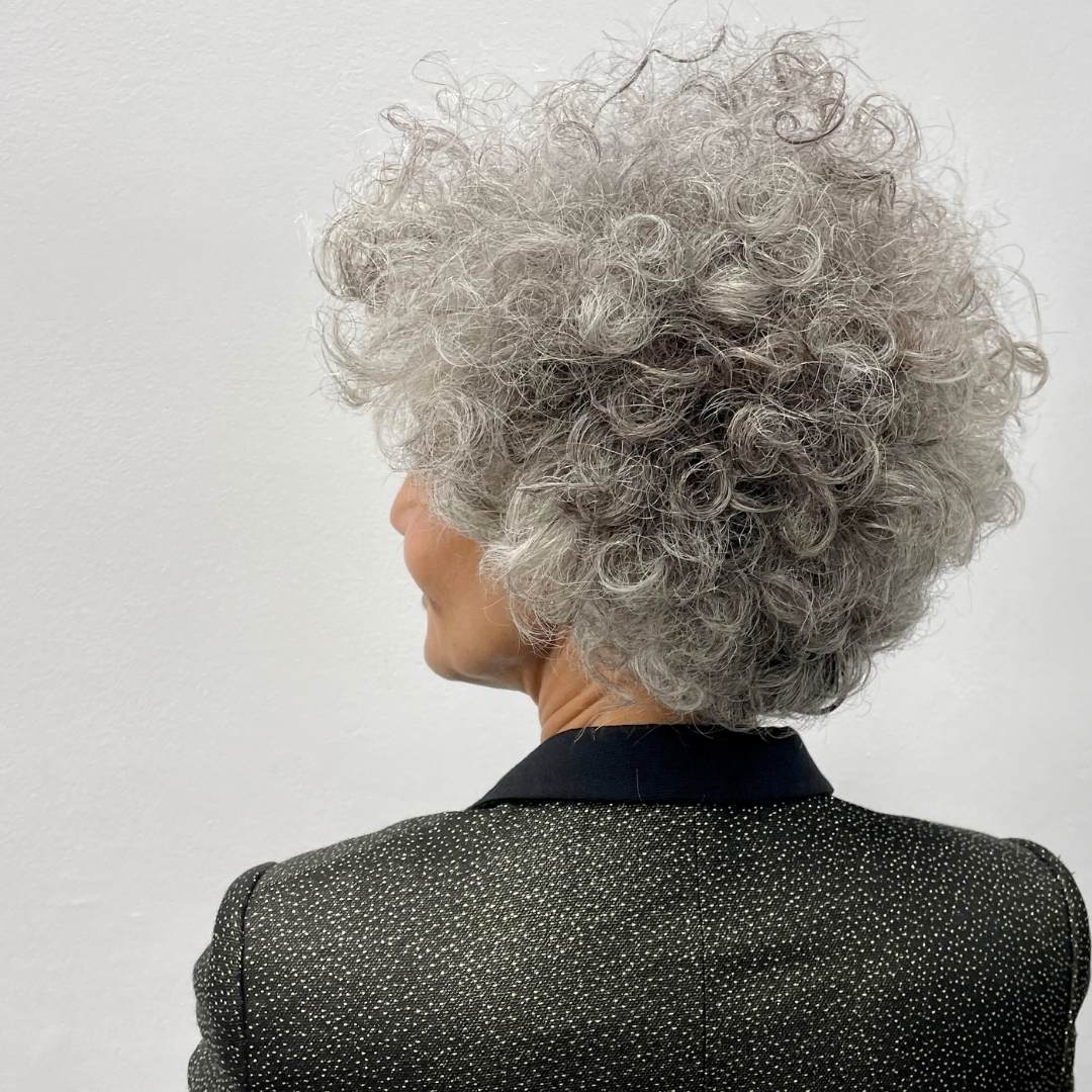 Person with grey curly hair wearing a black jacket against a light background