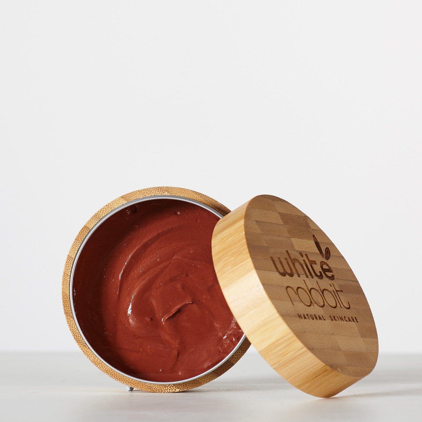 Open container of brown cream with wooden lid on a white background, featuring 'White Rabbit Natural Skincare' branding.