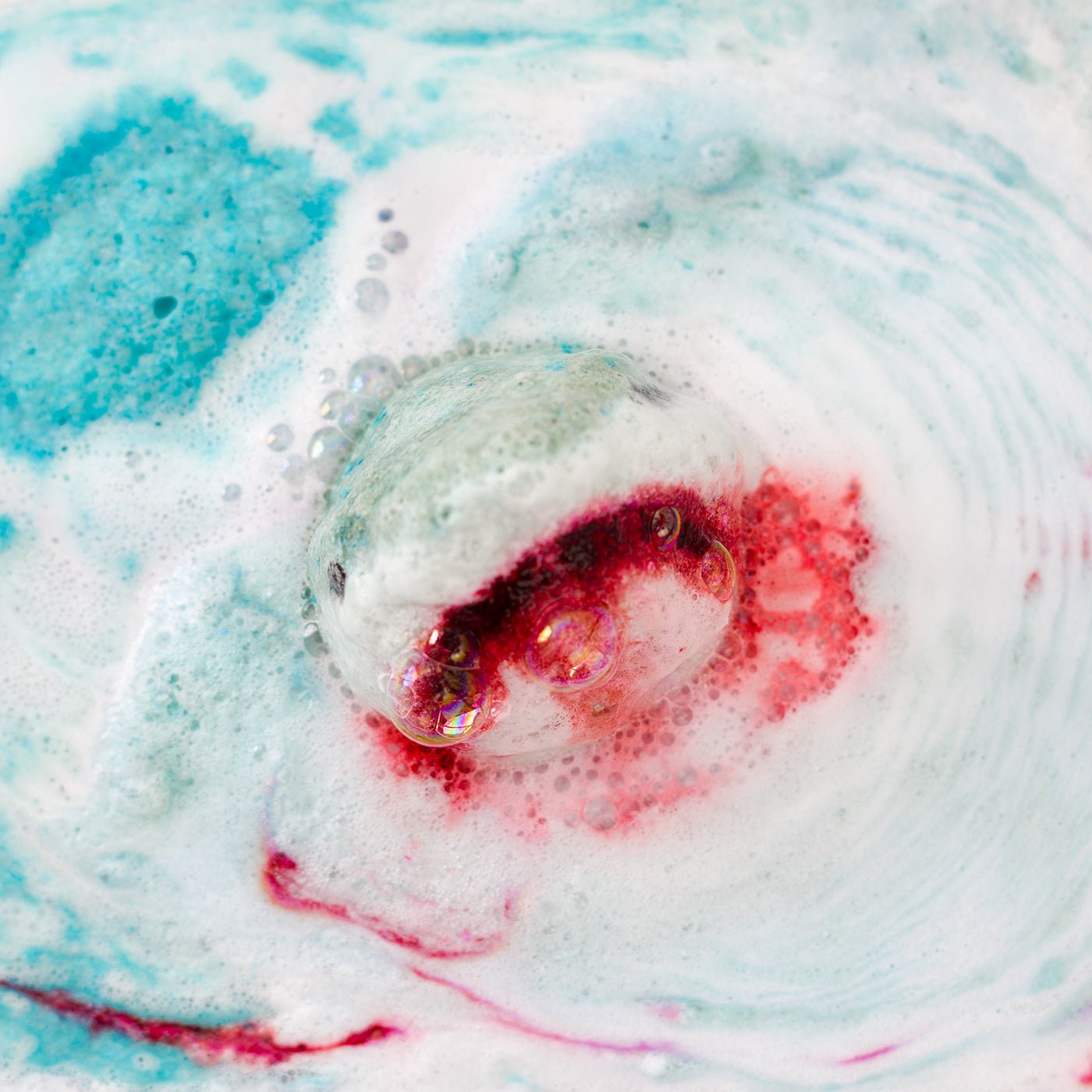 Close-up of a swirling bath bomb in water with blue, white, and red colours.