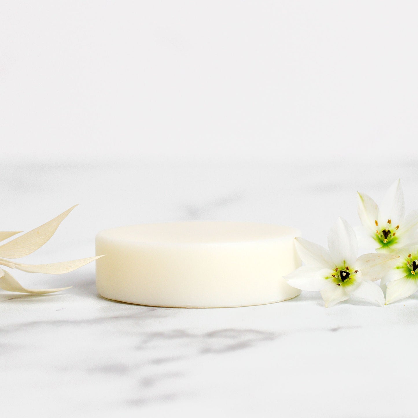White soap bar with a white flower on a light grey background