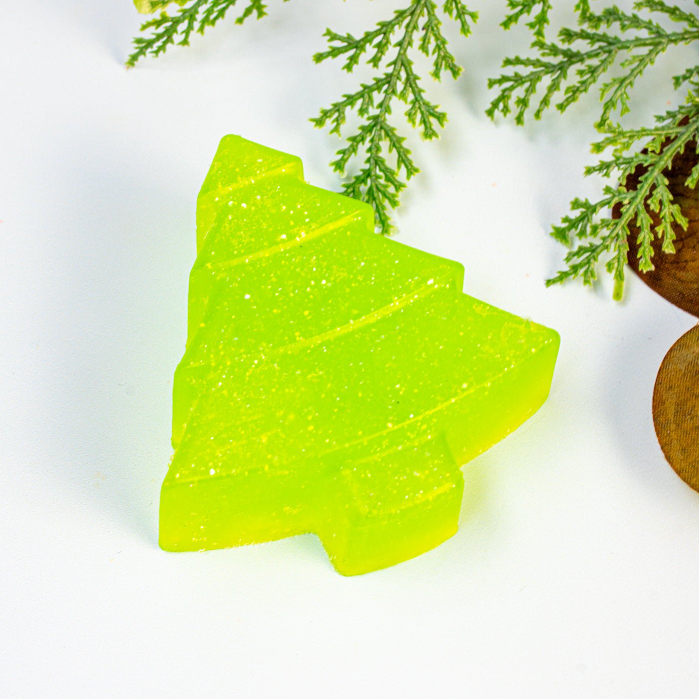 Green Christmas tree-shaped soap on a white background with greenery