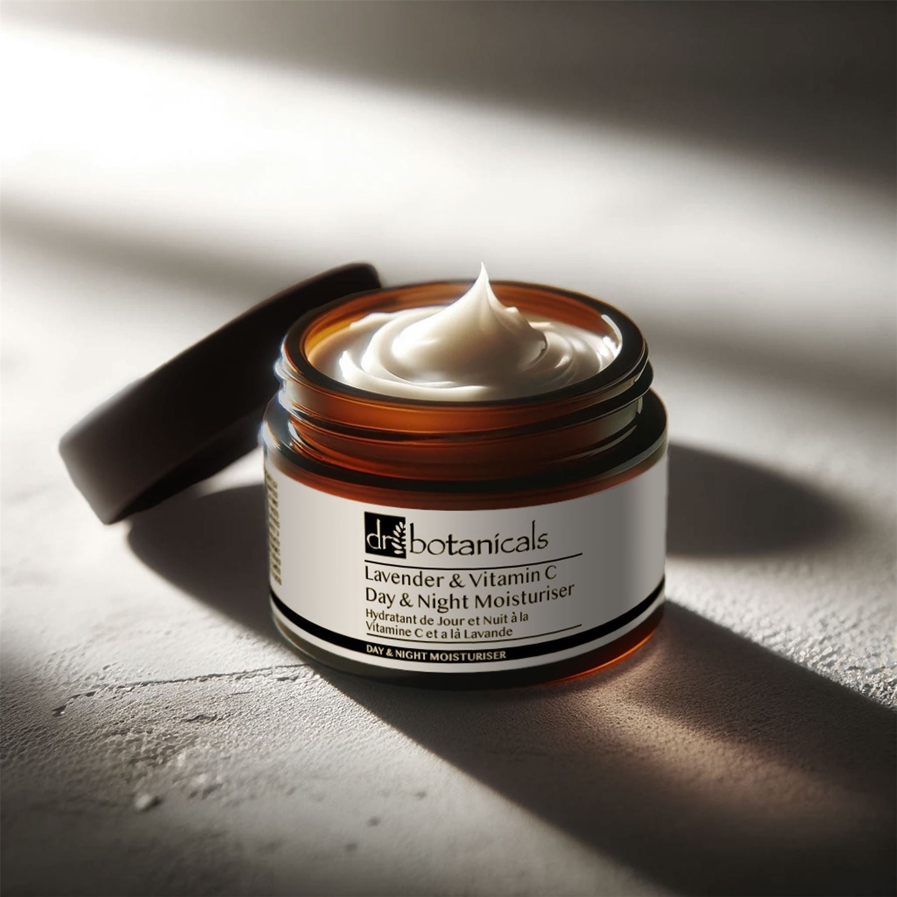 Open jar of Dr. Botanicals Lavender & Vitamin C Day & Night Moisturizer on a textured surface with soft lighting.