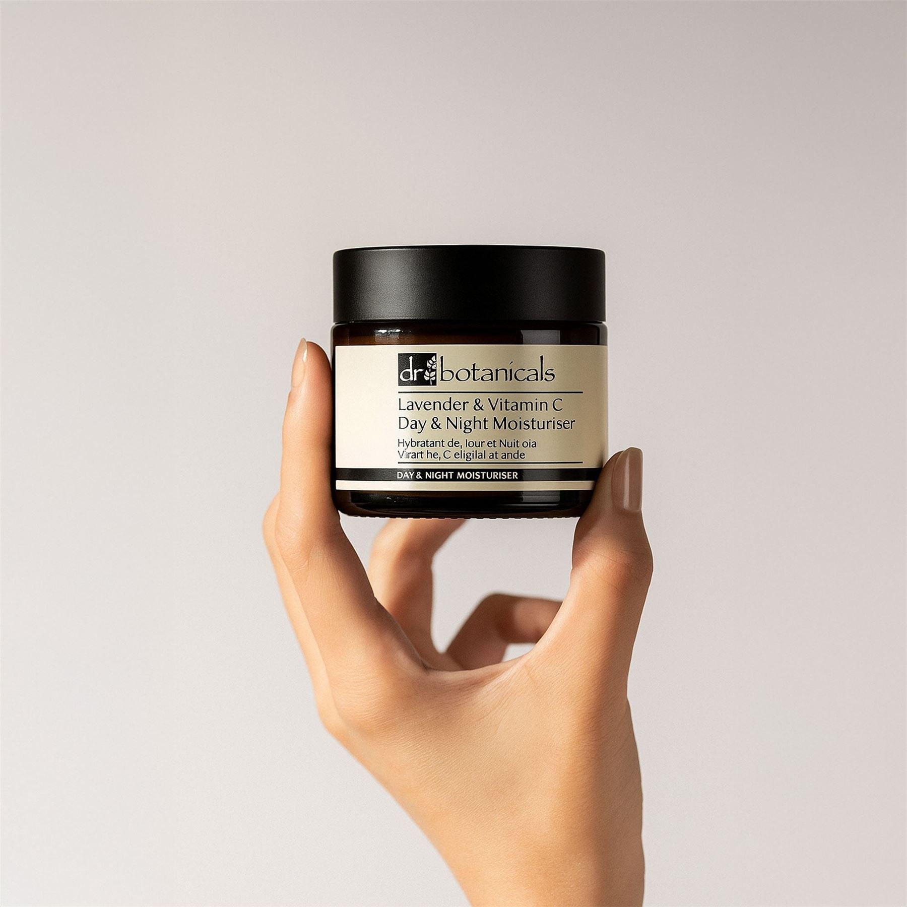 Hand holding a jar of 'Dr. Botanicals' day and night moisturizer against a plain background