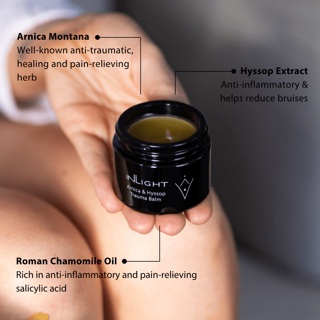 Hand holding a jar of Inlight Beauty Arnica & Hyssop Trauma Balm 45ml with text about its ingredients.