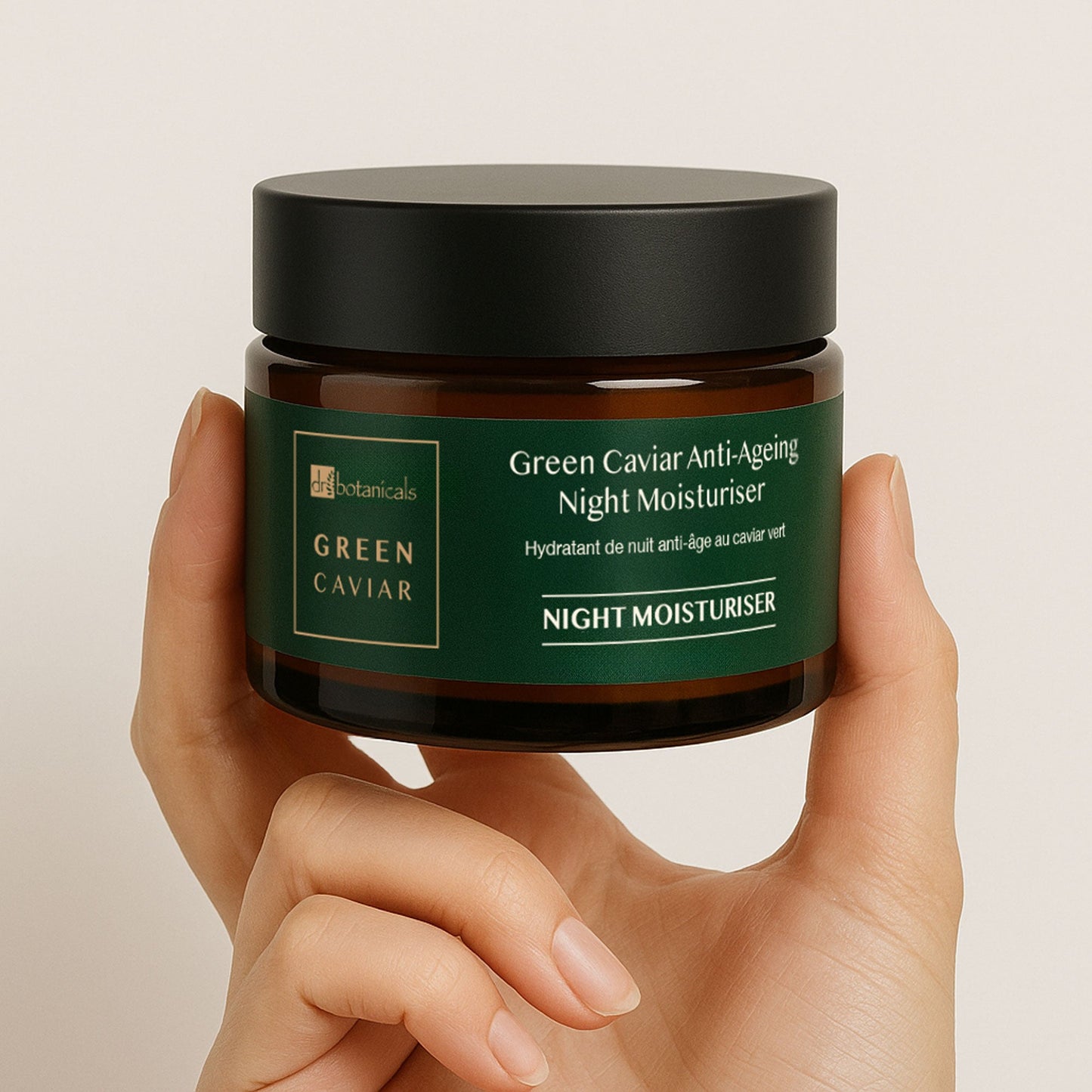 Hand holding a jar of Green Caviar Anti-Ageing Night Moisturiser against a beige background