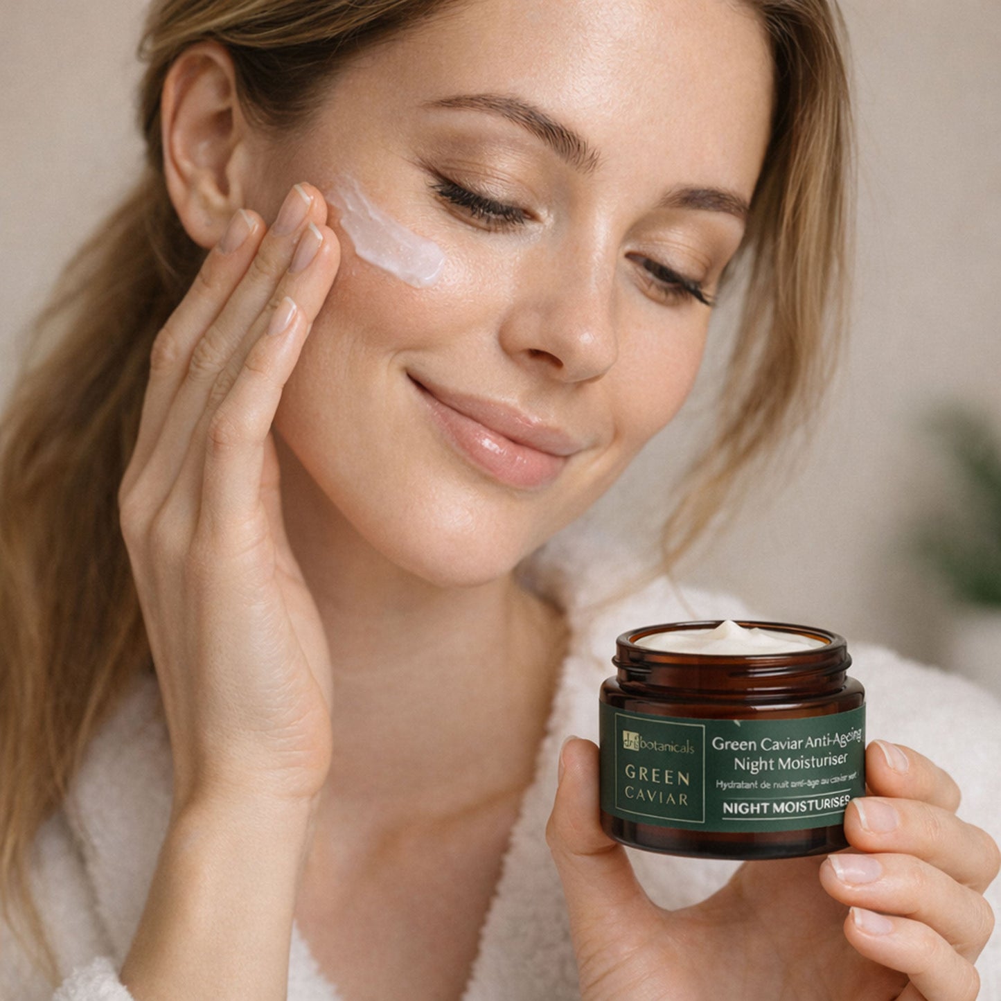 Woman applying cream to her face with a jar of Green Caviar Night Moisturizer.