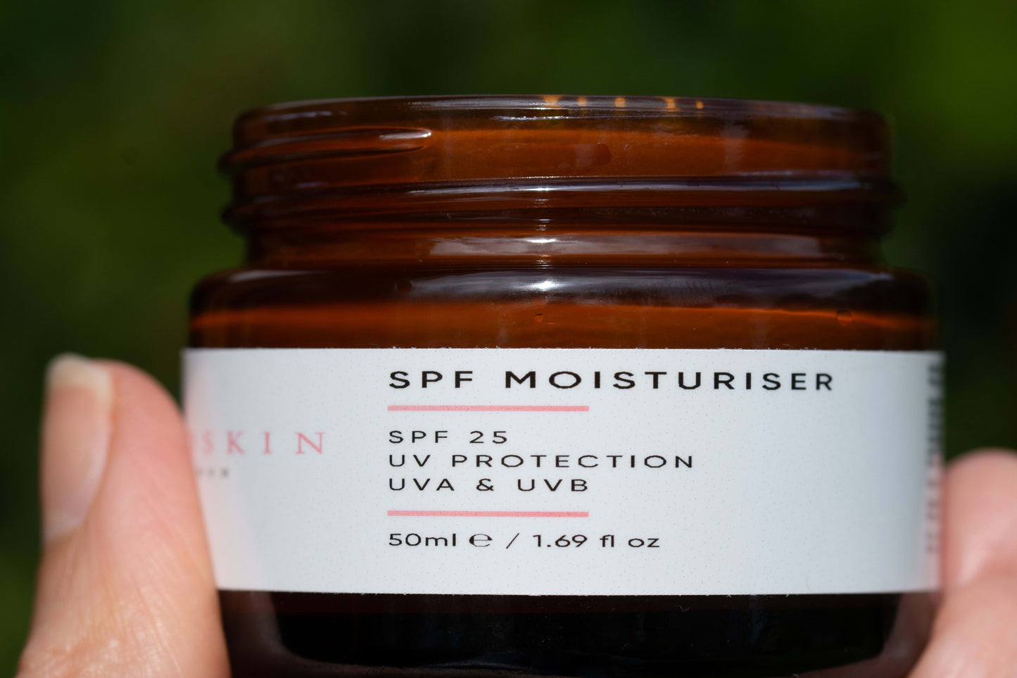 Jar of SPF moisturizer with a label on a blurred green background