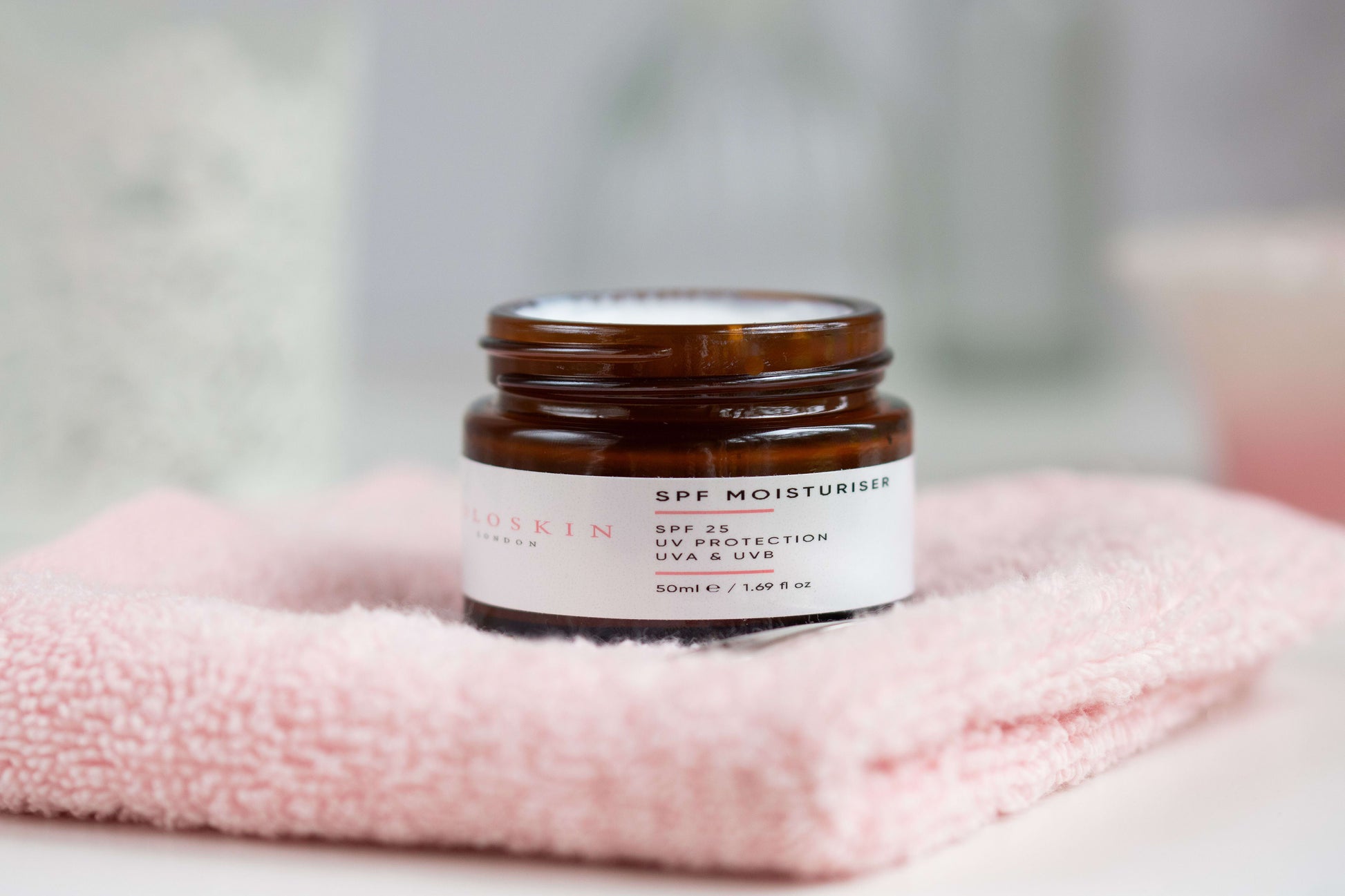 Jar of SPF moisturiser on a pink towel with a blurred background