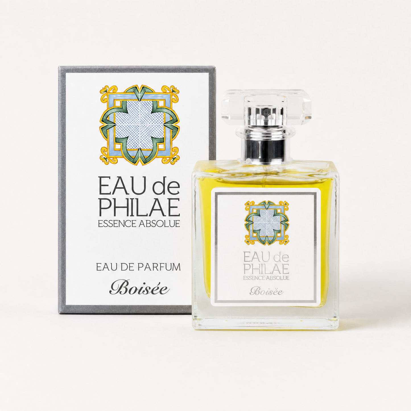 A bottle of Inlight Beauty Eau de Parfum Boisée for Him 50ml next to its original packaging box, both featuring a white label with a blue and green geometric cross design and gold accents, set against a clean white background.