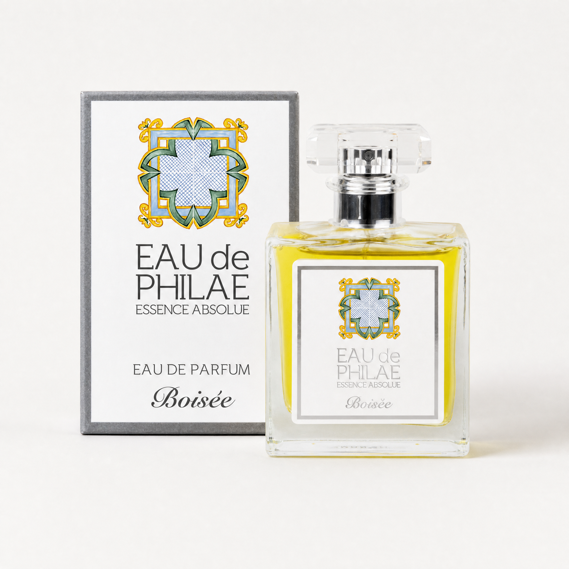 A bottle of Inlight Beauty Eau de Parfum Boisée for Him 50ml next to its original packaging box, both featuring a white label with a blue and green geometric cross design and gold accents, set against a clean white background.