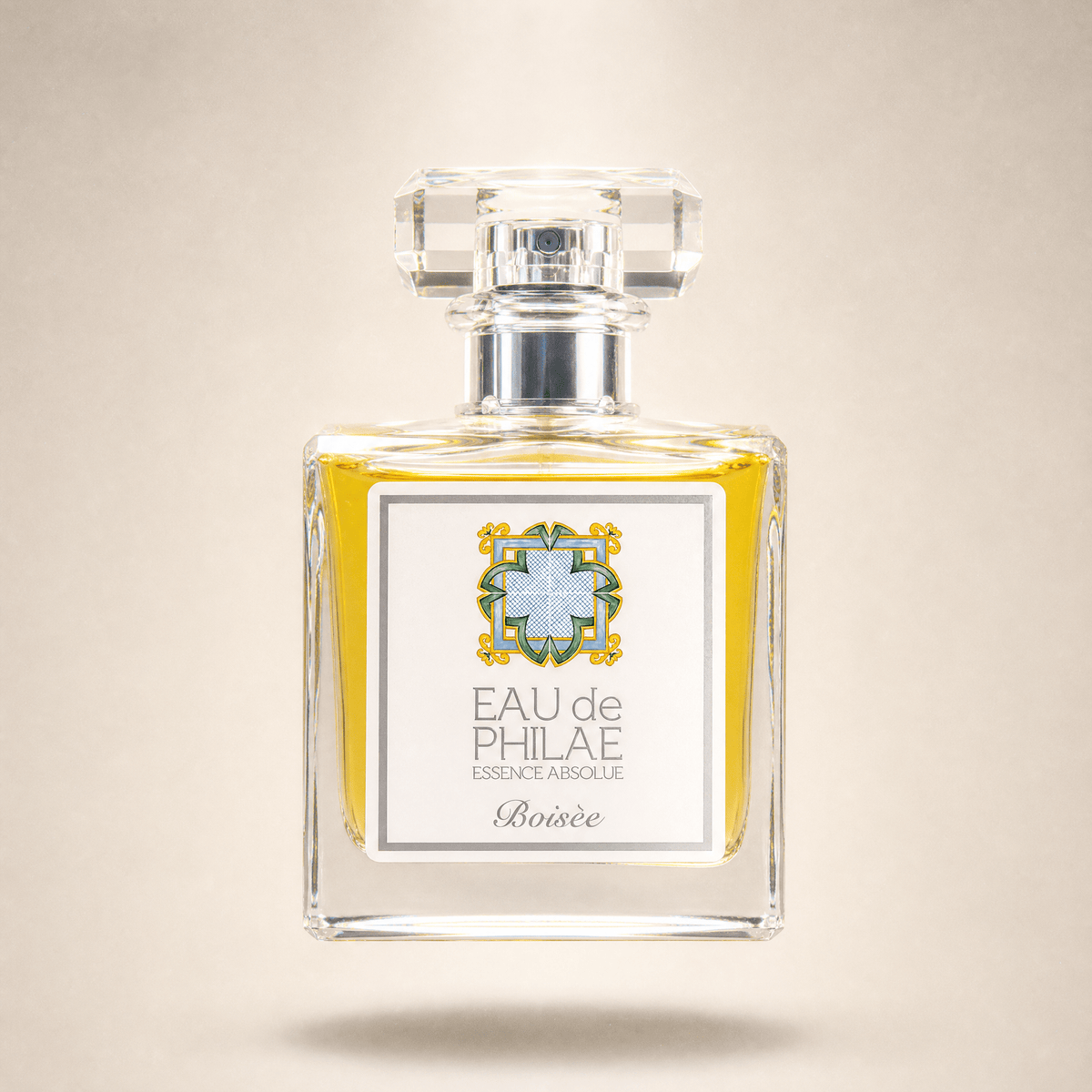 A square glass perfume bottle with a clear faceted cap, filled with yellow liquid and featuring a white label with the text 'EAU de PHILAE ESSENCE ABSOLUE Boisée'.