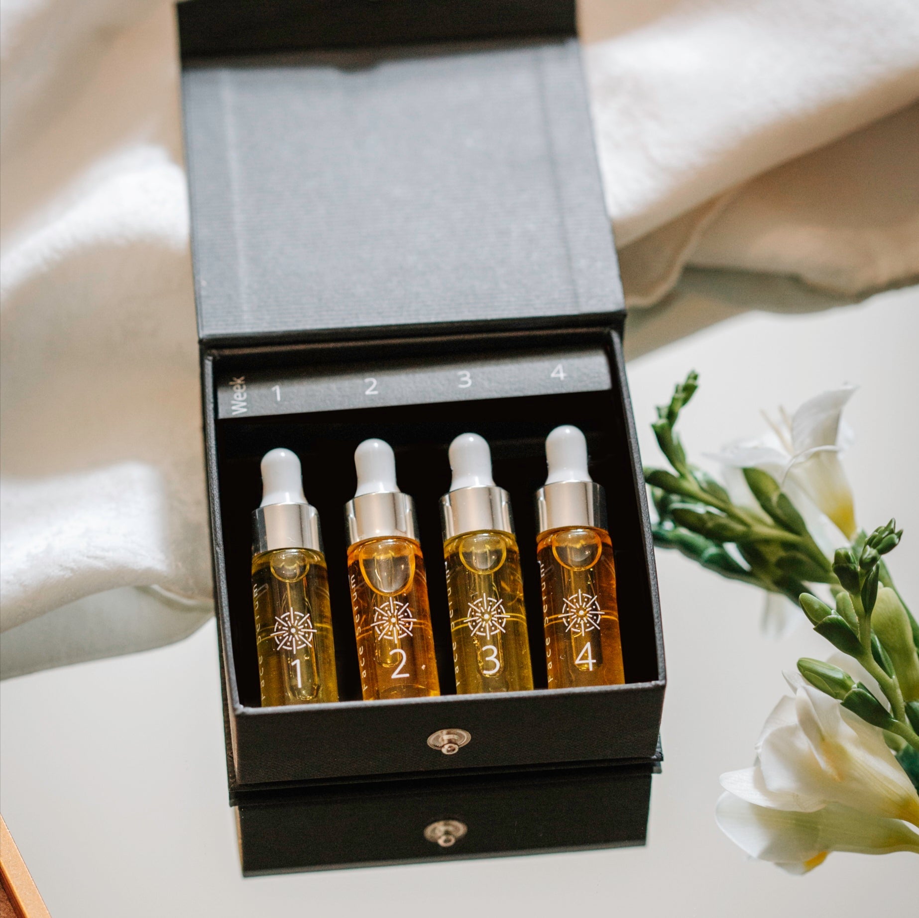 Set of four dropper bottles of Inlight Beauty Supreme Face Serum 4 x 4.9ml with a floral arrangement in the background