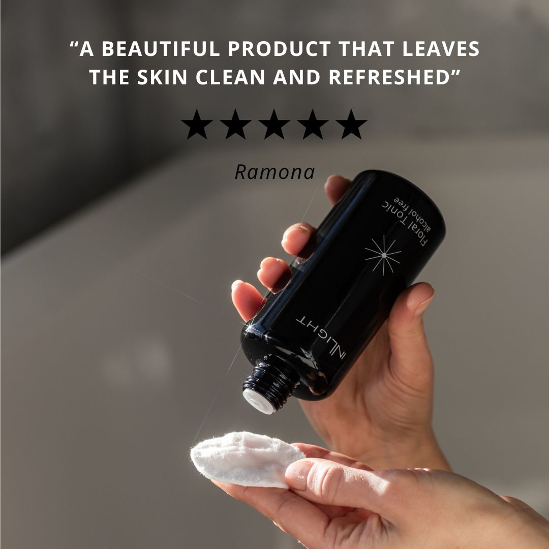 Hand holding a black bottle of Inlight Beauty Floral Tonic 200ml product with a white cloth, against a neutral background.