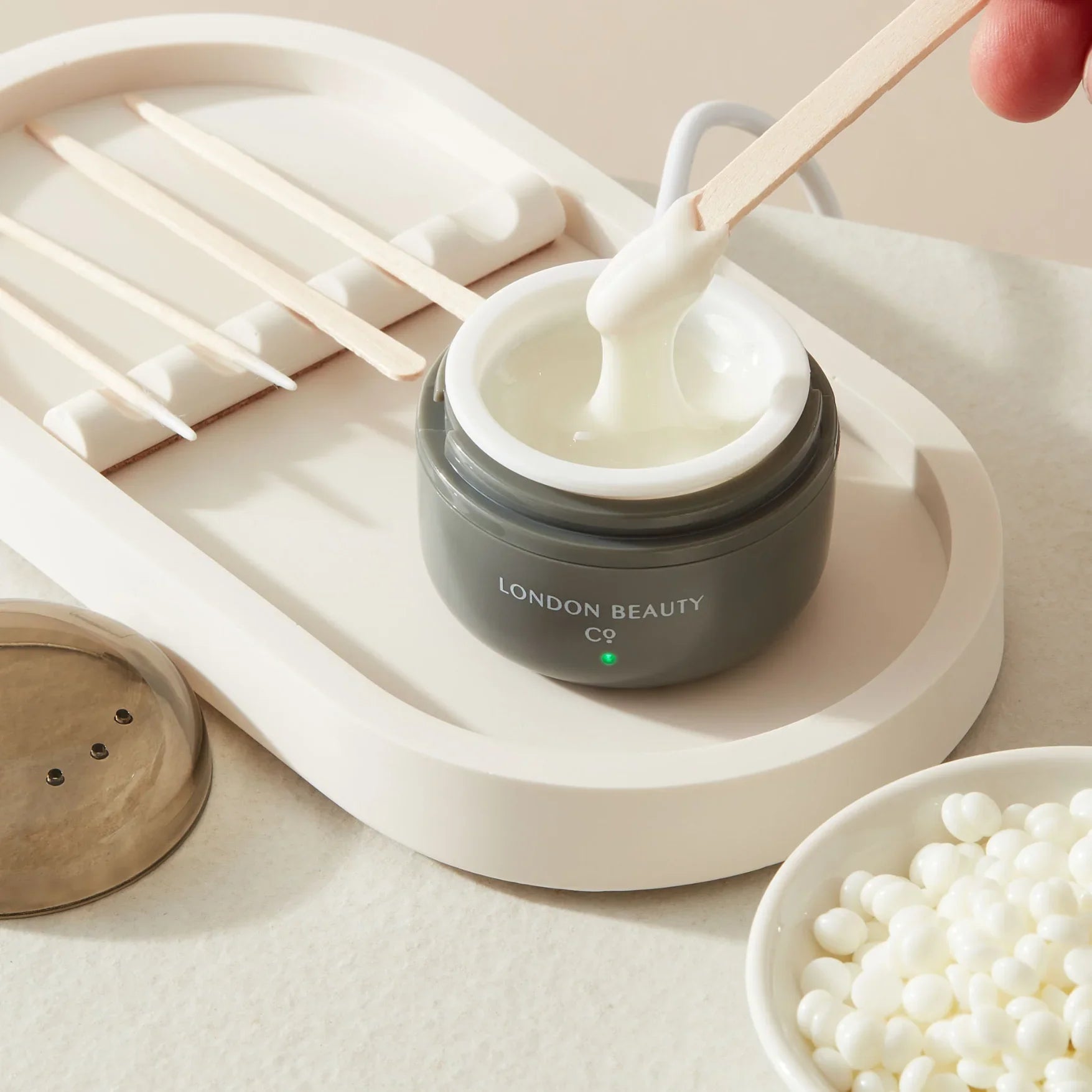 Jar of Wax labeled 'London Beauty' with a wooden stick, on a neutral background.