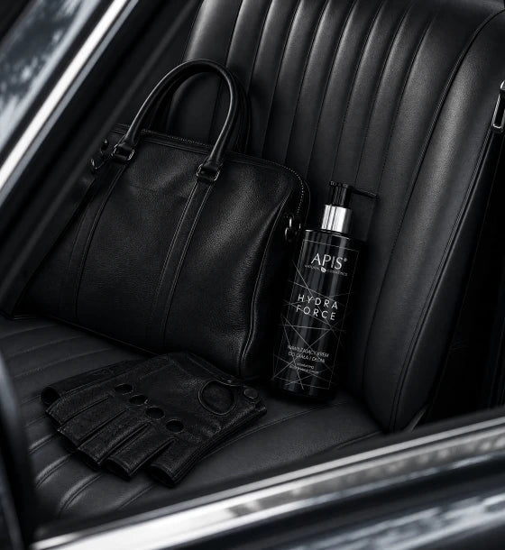 A black leather handbag and matching black fingerless gloves rest on a black car seat beside a black APIS Hydra Force bottle, photographed in a car interior.