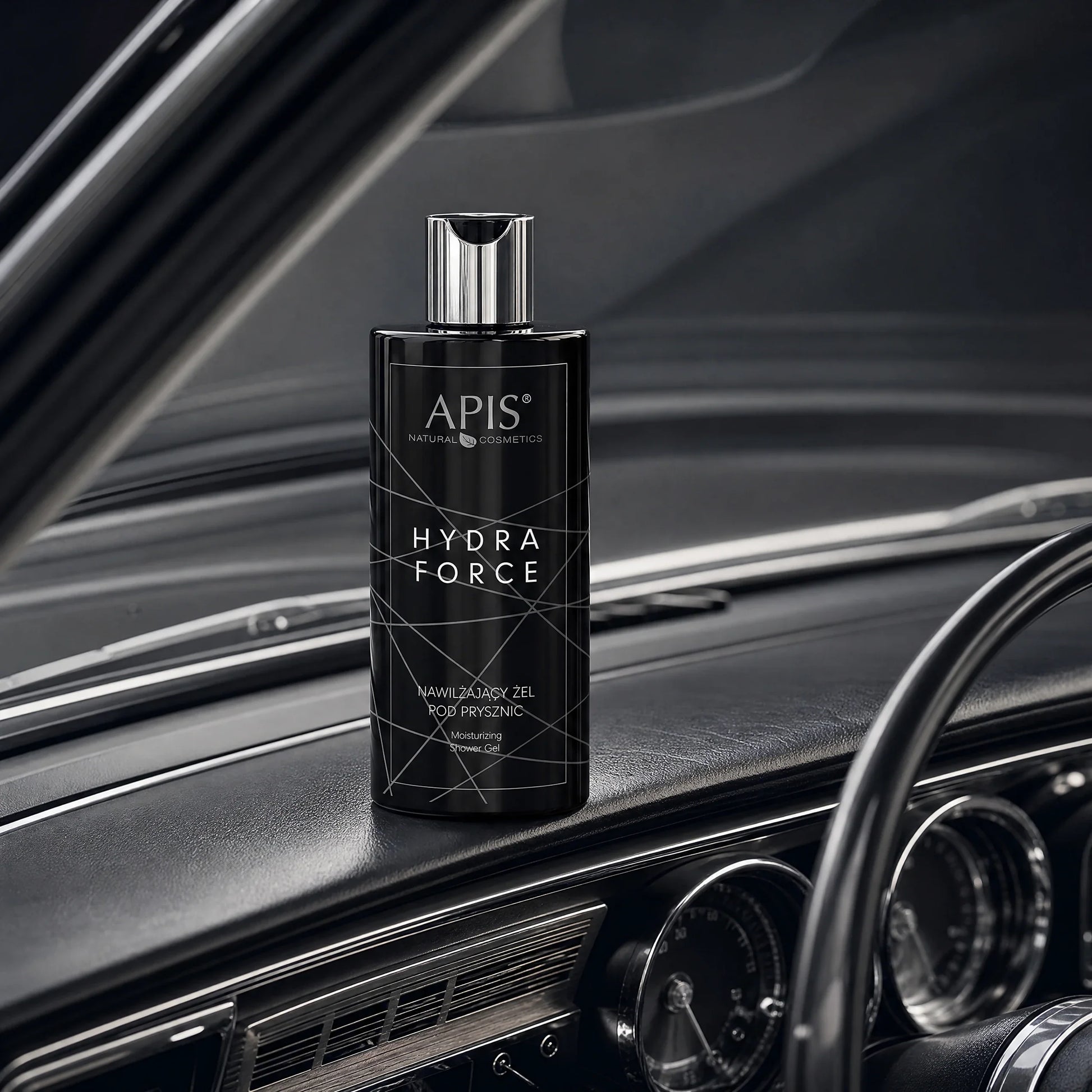 A bottle of Apis Hydra Force Moisturising Shower Gel for Men 300ml placed on the dashboard of a classic car, with the steering wheel and instrument gauges visible in the background.