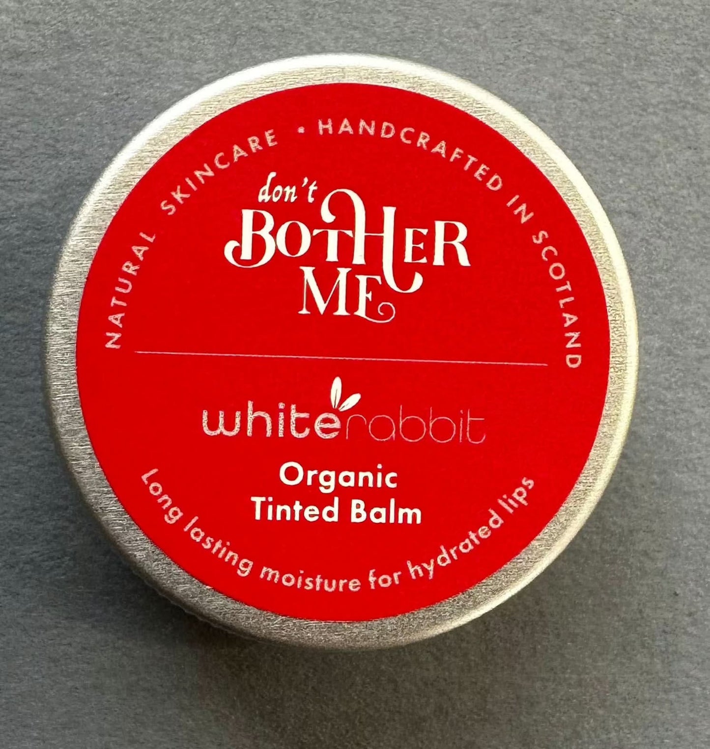 Red and silver container of 'don't BOTHER ME' organic tinted balm on a grey background