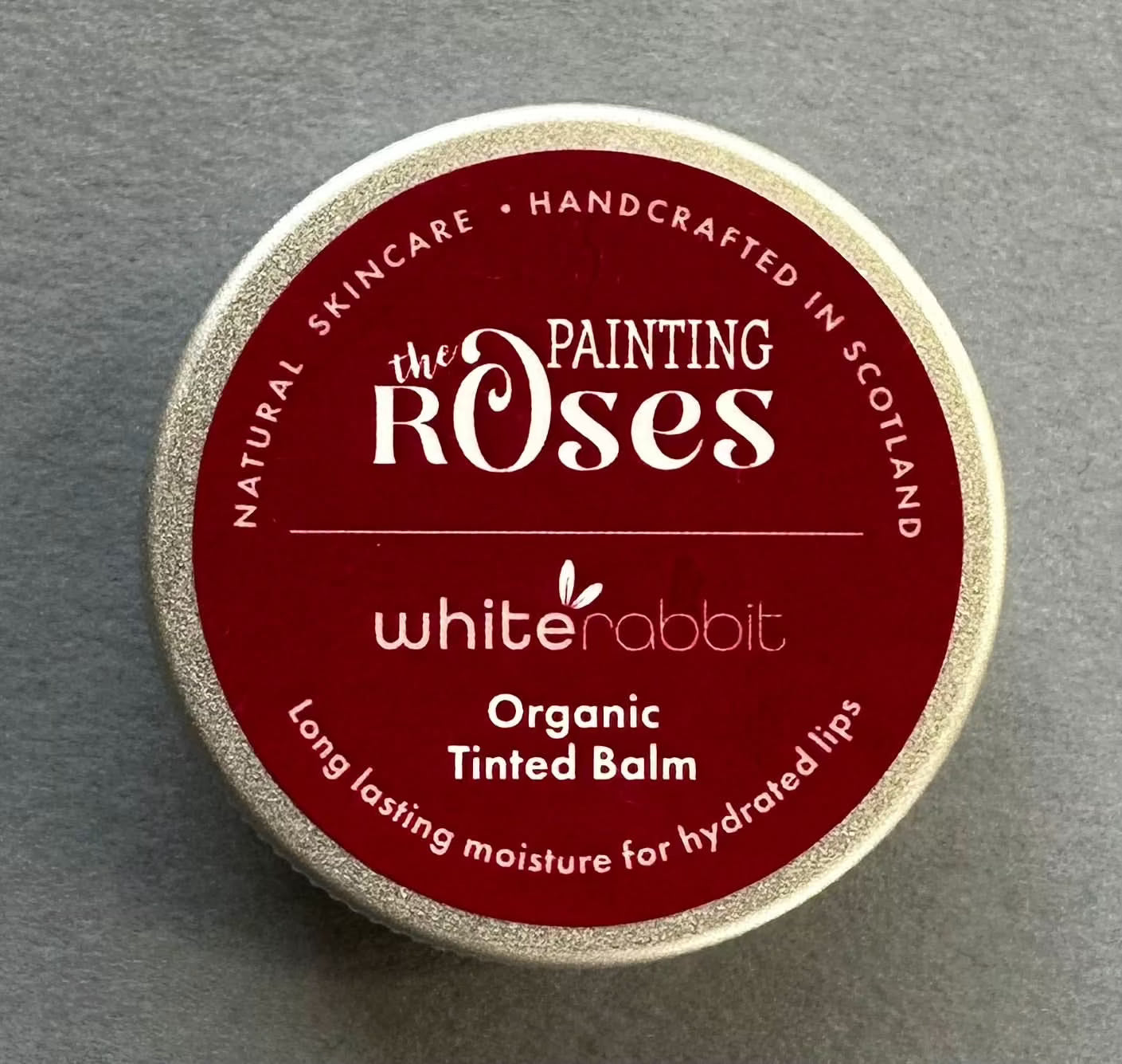 Tin of 'The Painting Roses' white rabbit organic tinted balm on a grey background