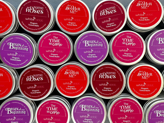 Collection of tins of White Rabbit Organic Tinted Lip & Cheek Balm with various labels arranged in a pattern