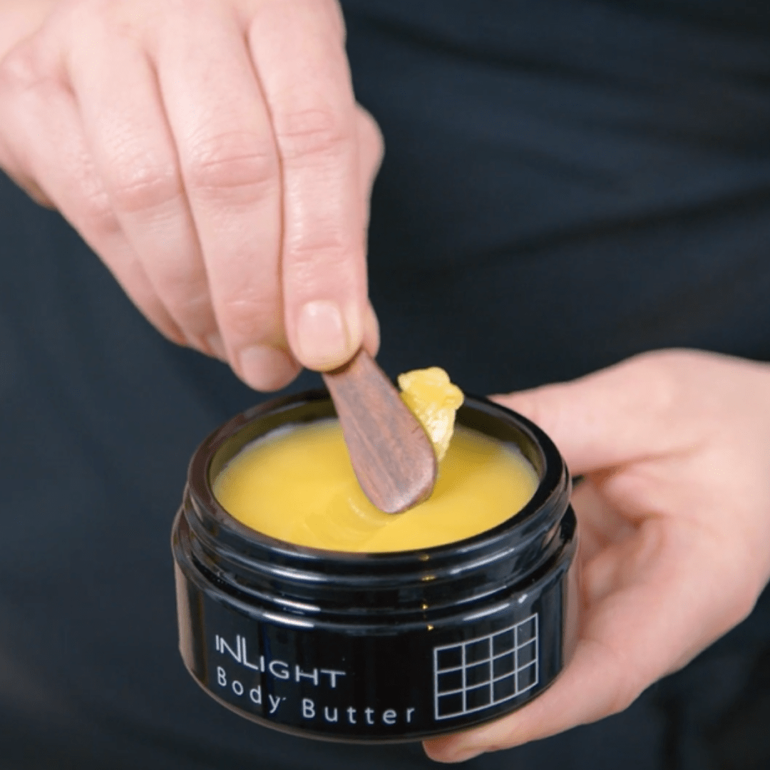 Person using a spatula to take body butter from a jar labeled Inlight Beauty Body Butter 90ml