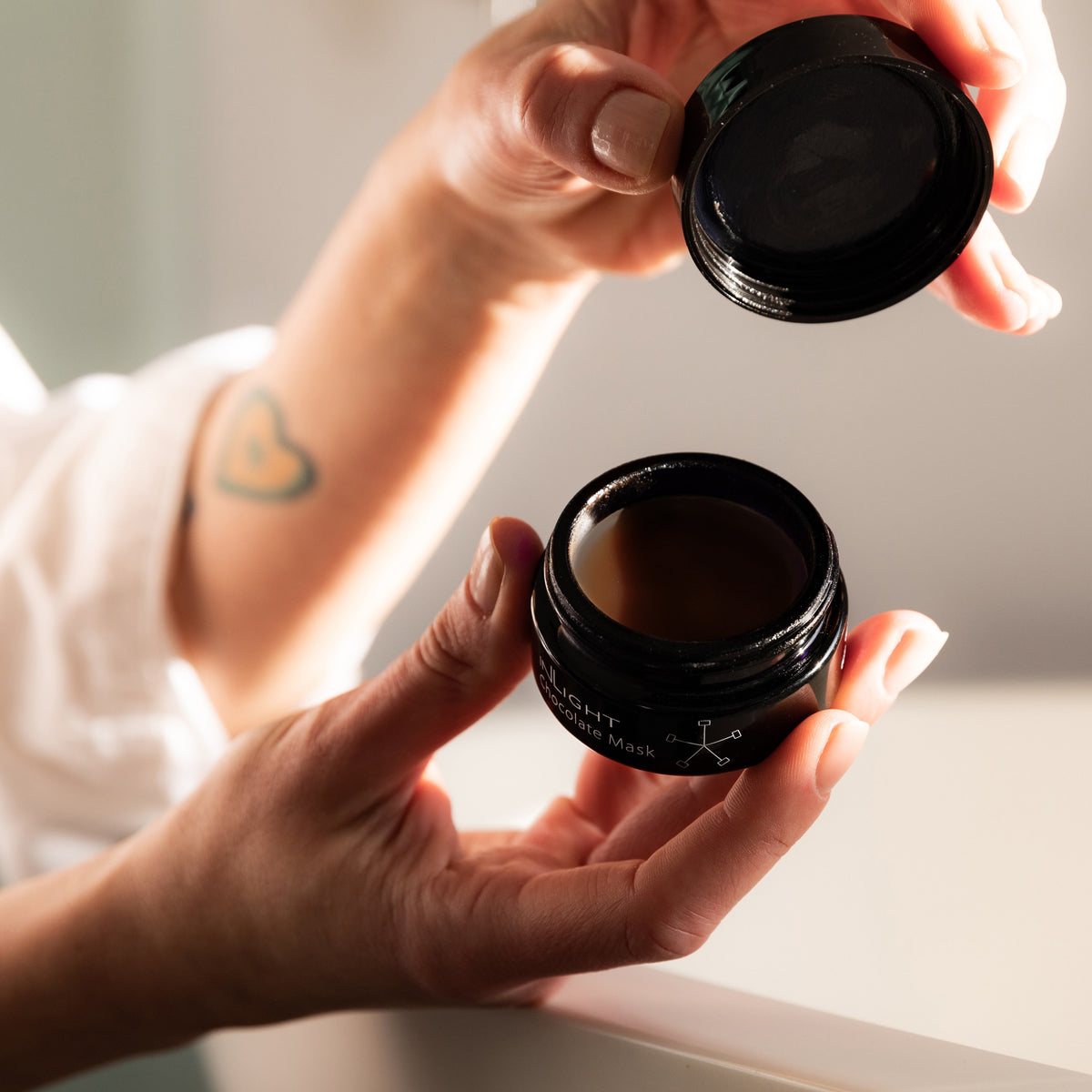 Person holding a black jar with a lid, showing its contents, Inlight Beauty Chocolate Mask 25ml
