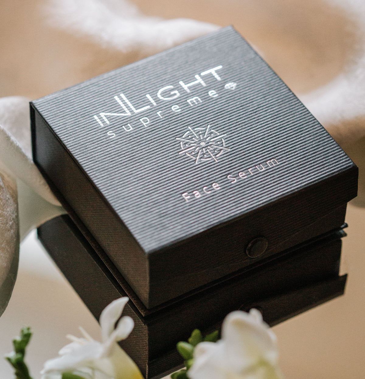 Inlight Beauty Supreme Face Serum 4 x 4.9ml packaging on a reflective surface with flowers in the background