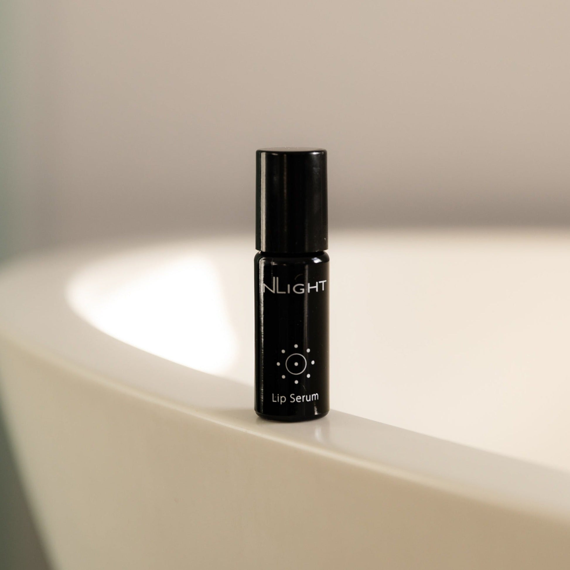 Black lip serum bottle labeled 'InLight' on a light surface with a neutral background