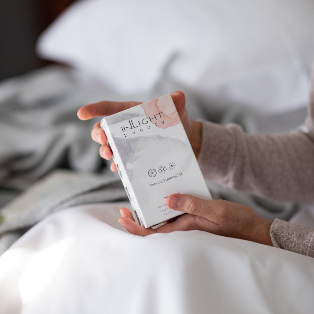 Person holding an 'INLIGHT beauty' product packaging in a bedroom setting
