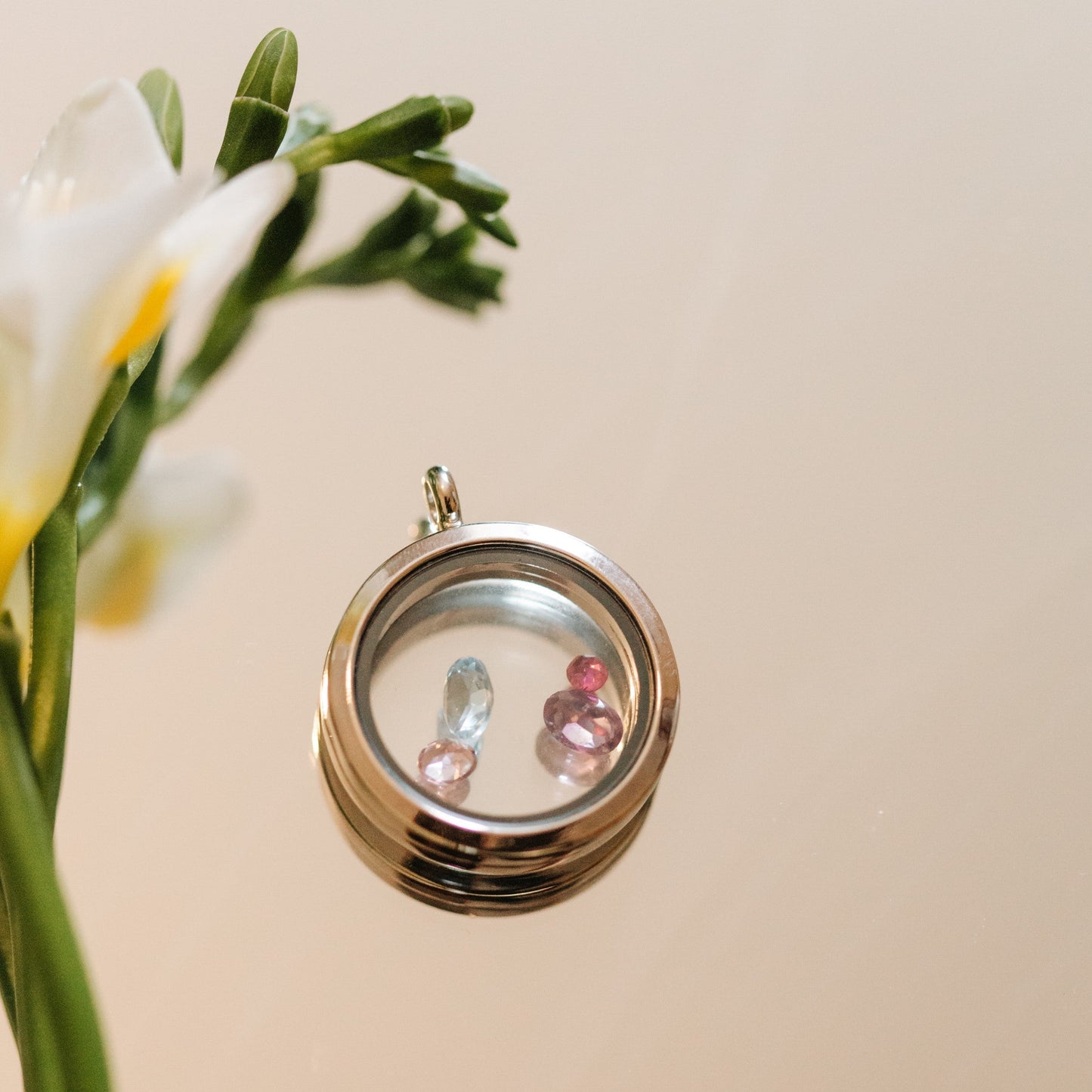 Silver locket with embedded gemstones next to a bouquet of flowers on a beige background