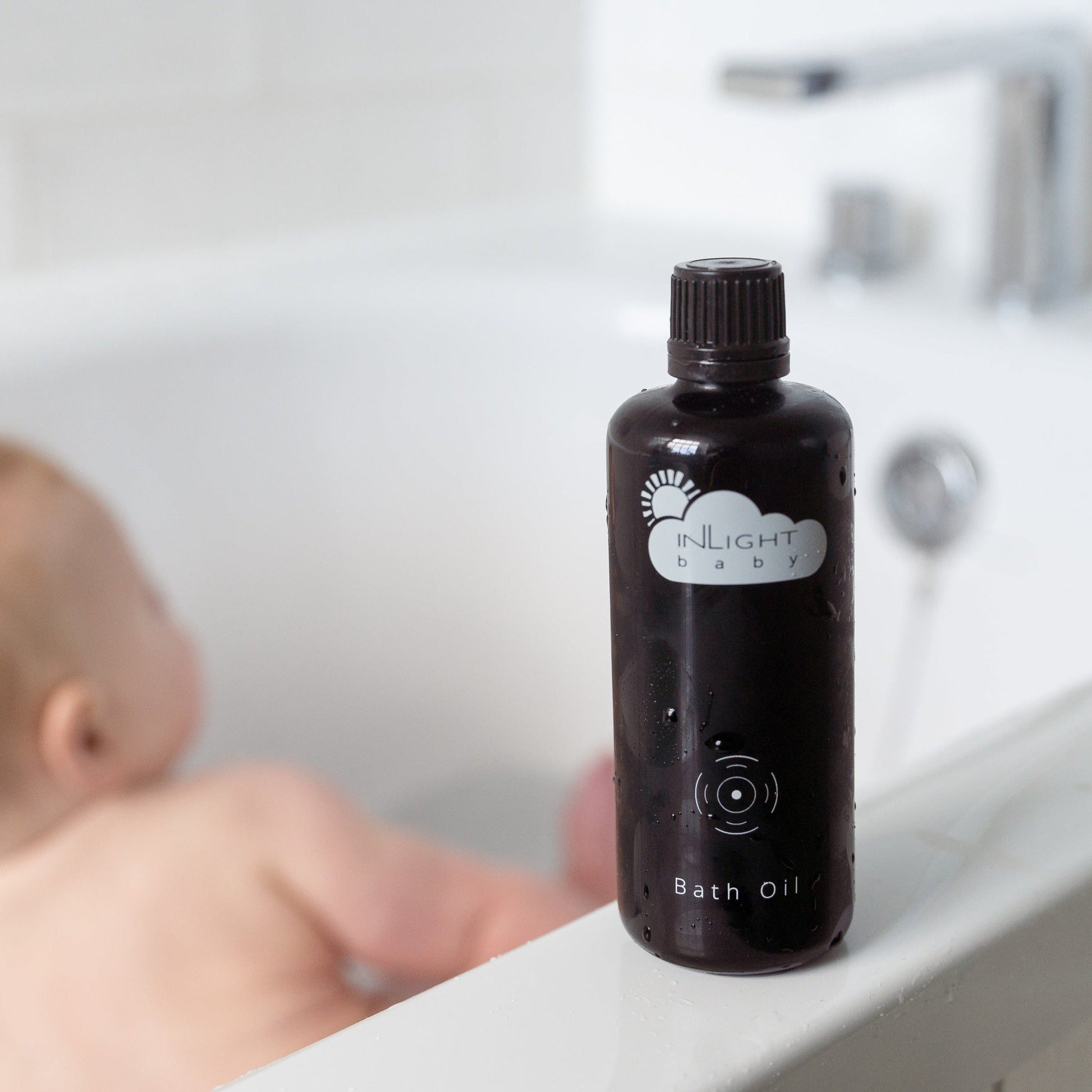 Bottle of Inlight Beauty Baby Bath Oil 100ml on a bathtub ledge with a blurred child in the background