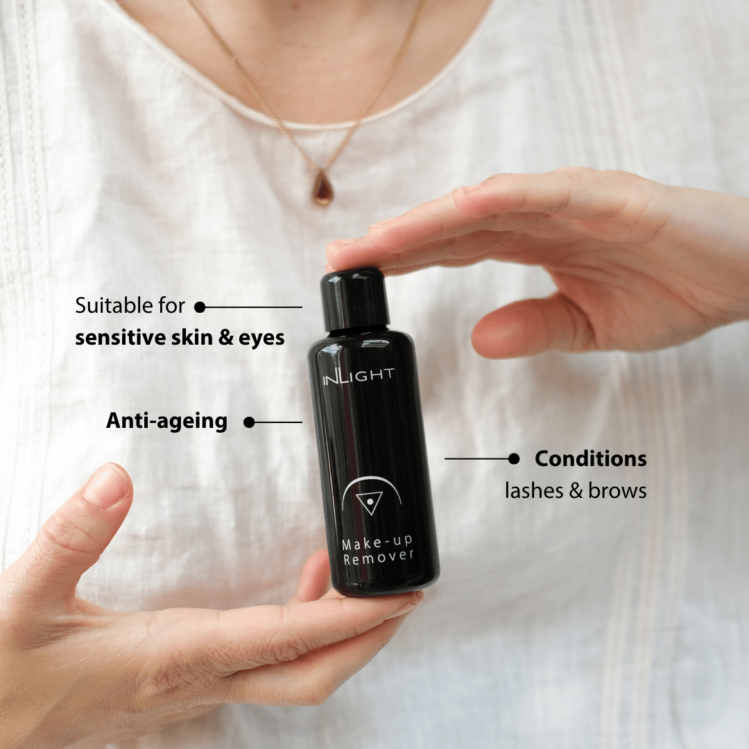 Person holding a black bottle of Inlight Beauty Make-up Remover Oil 50ml with text on its suitability for sensitive skin, anti-ageing, and conditions lashes and brows.