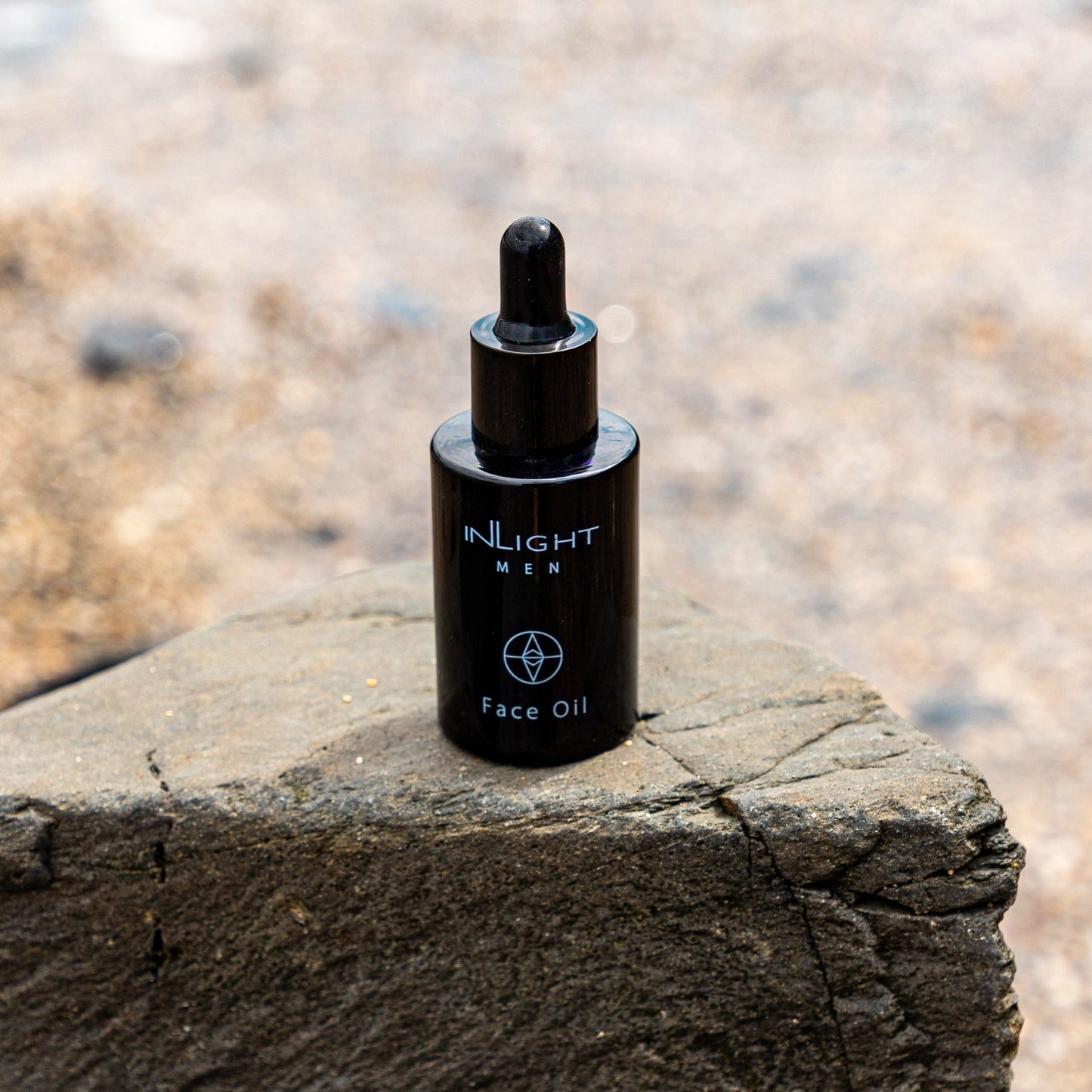 Black bottle of Inlight Beauty Face Oil for Men 30ml on a stone surface with a blurred natural background