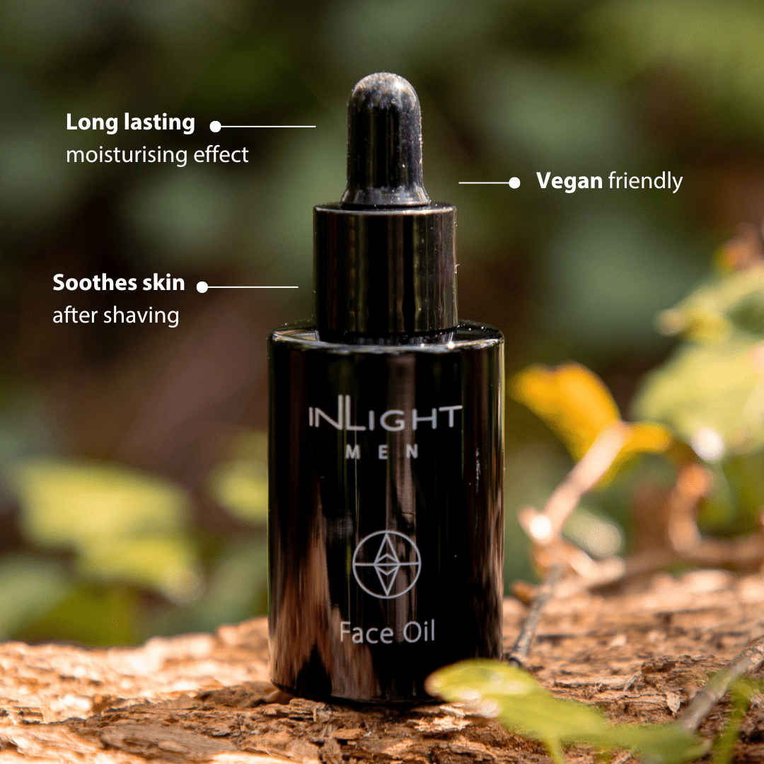 Black bottle of Inlight Beauty Face Oil for Men 30ml on a wooden surface with greenery in the background