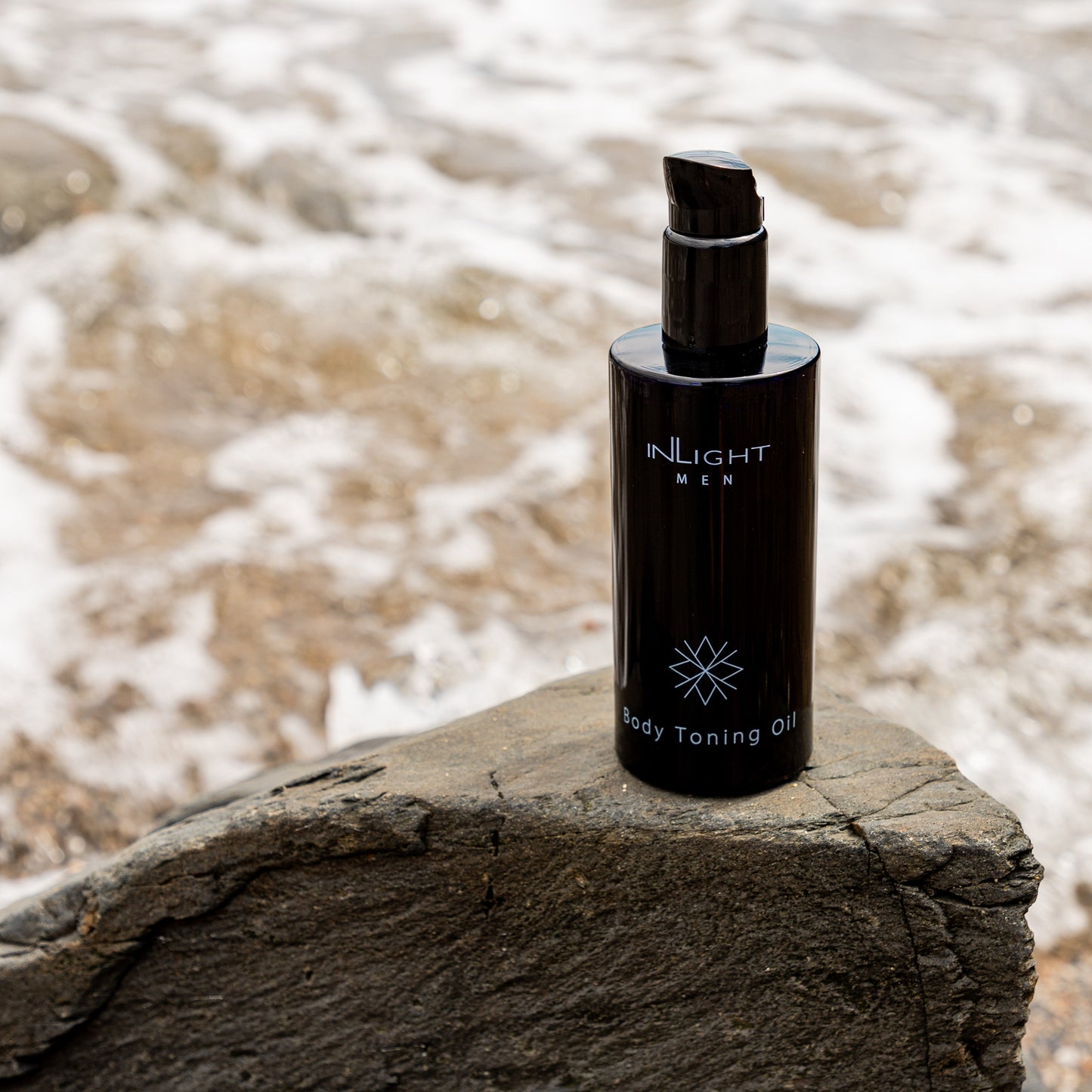 Black bottle of Inlight Beauty Body Toning Oil for Men 200ml on a rock with water in the background