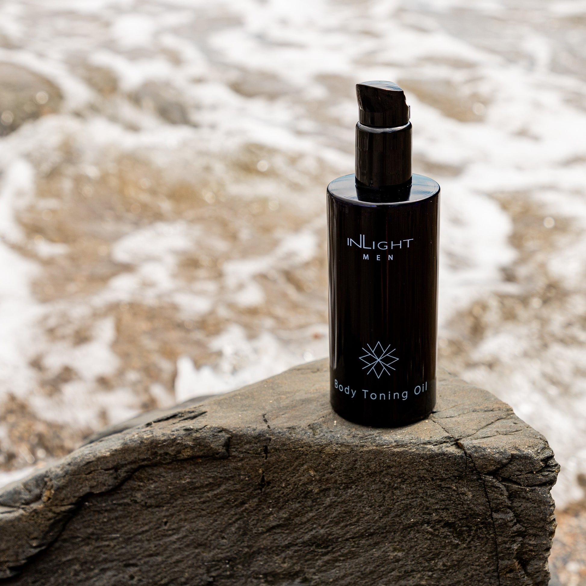 Black bottle of Inlight Beauty Body Toning Oil for Men 200ml on a rock with water in the background