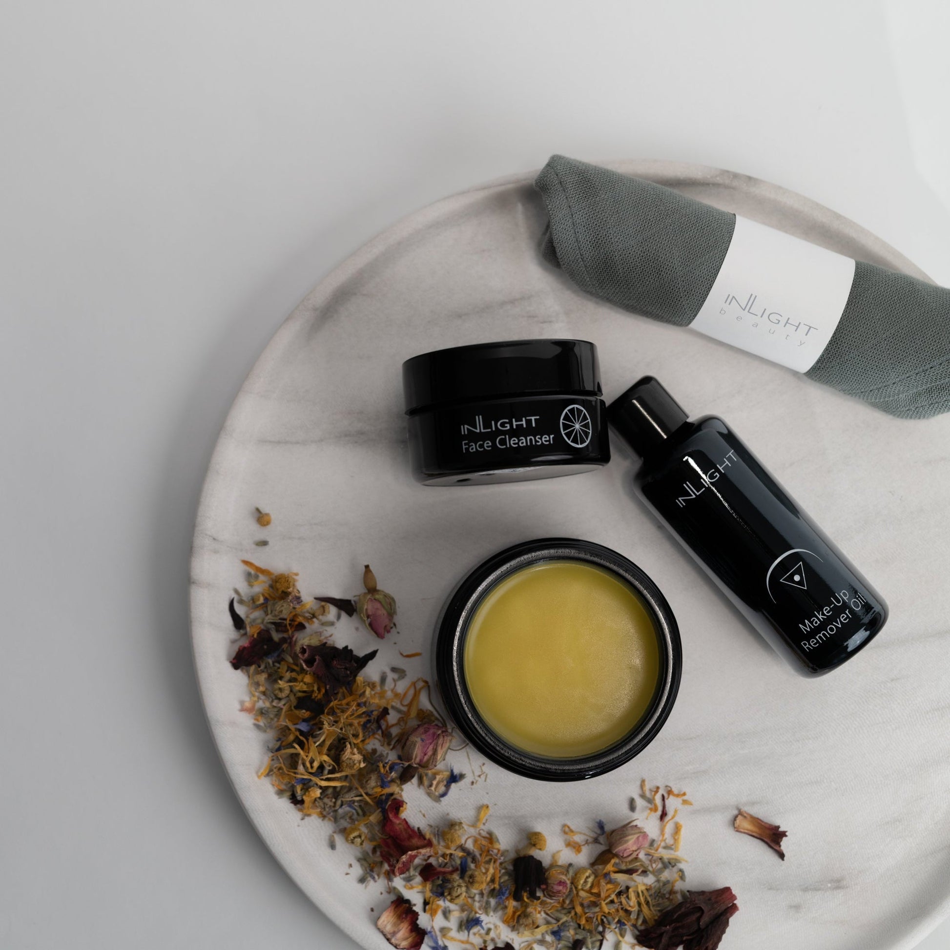Skincare products including Inlight Beauty Make-up Remover Oil 50ml on a marble tray with dried flowers