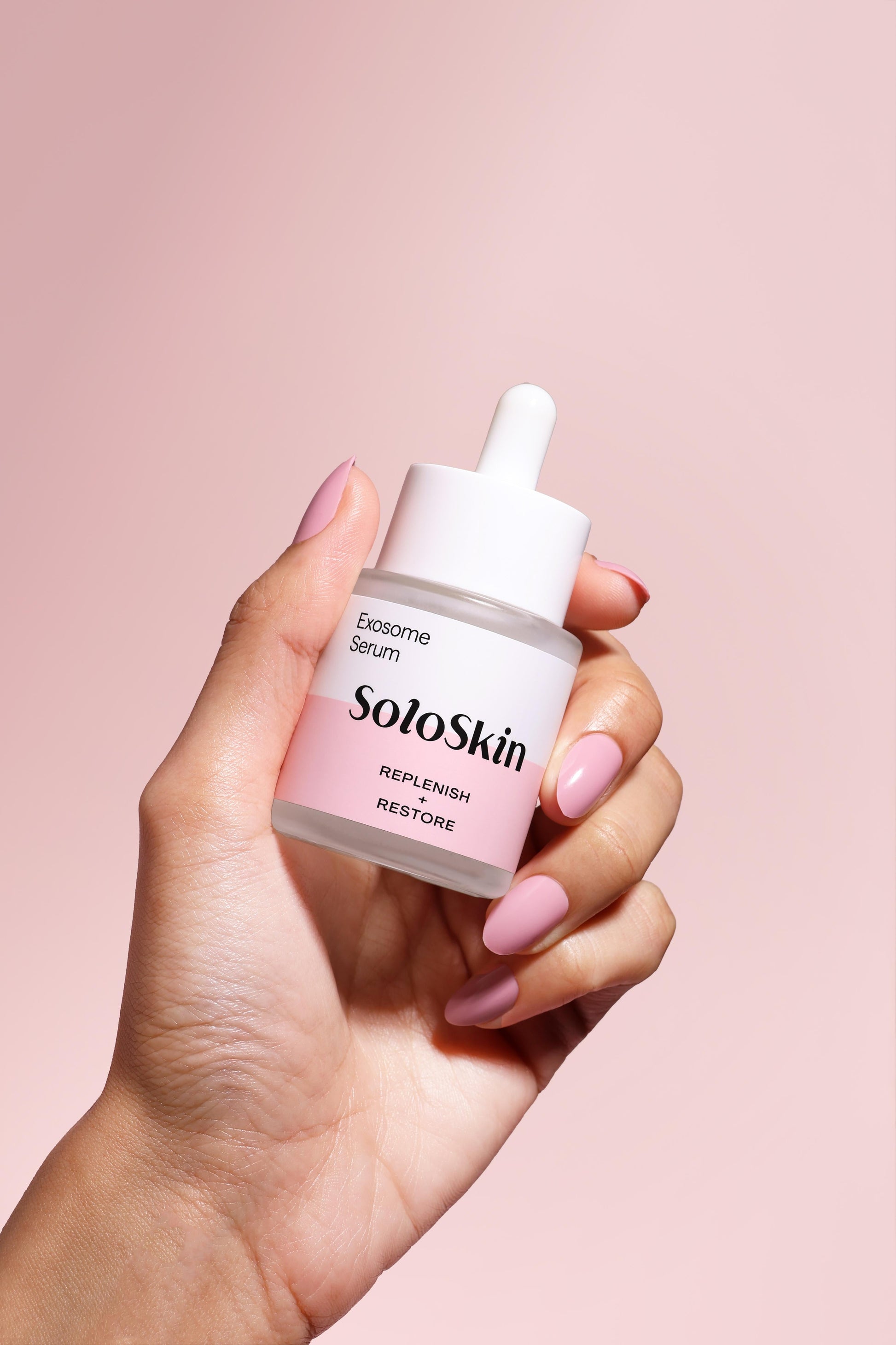 Hand holding a bottle of SoloSkin serum against a pink background