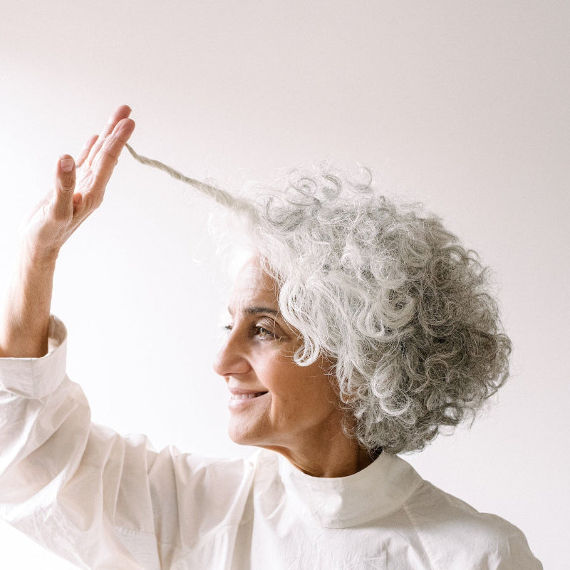 Woman with grey hair touching her hair against a white background