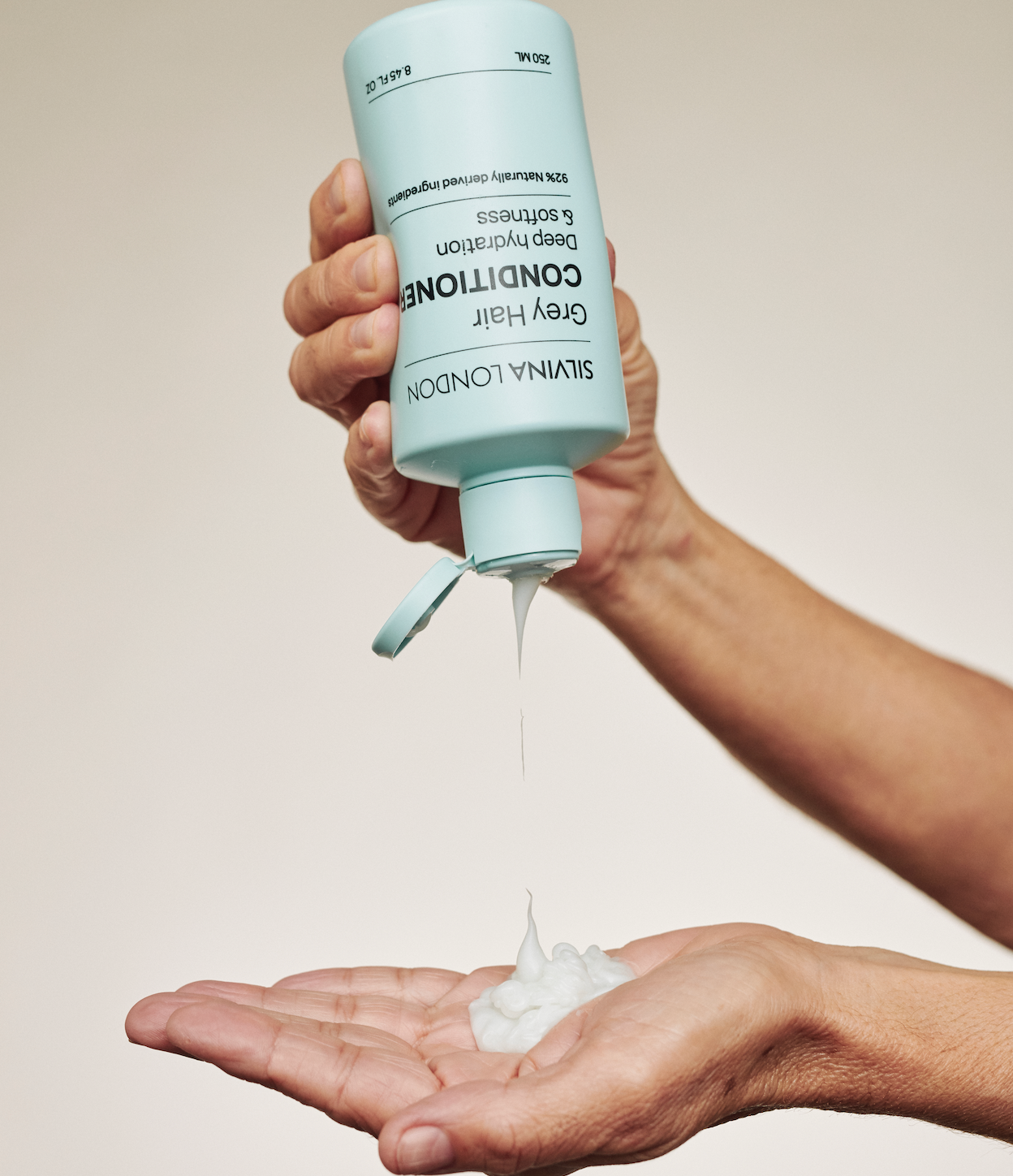 Person pouring a blue bottle of Silvina London conditioner into their hand against a neutral background
