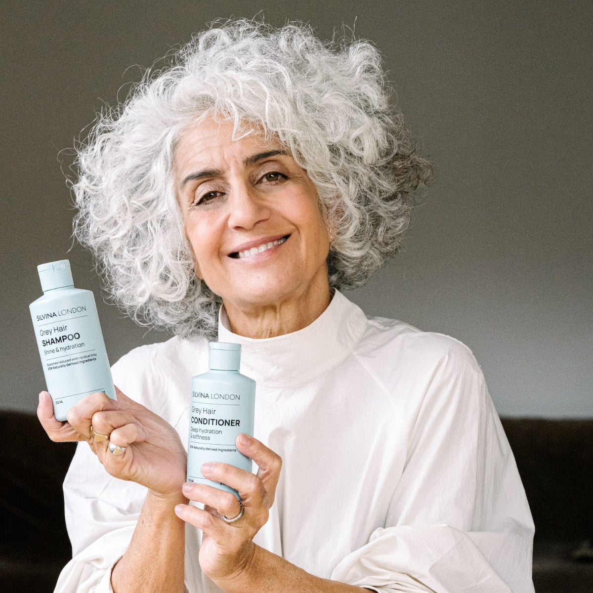 Woman holding two bottles of shampoo and conditioner, with a neutral background