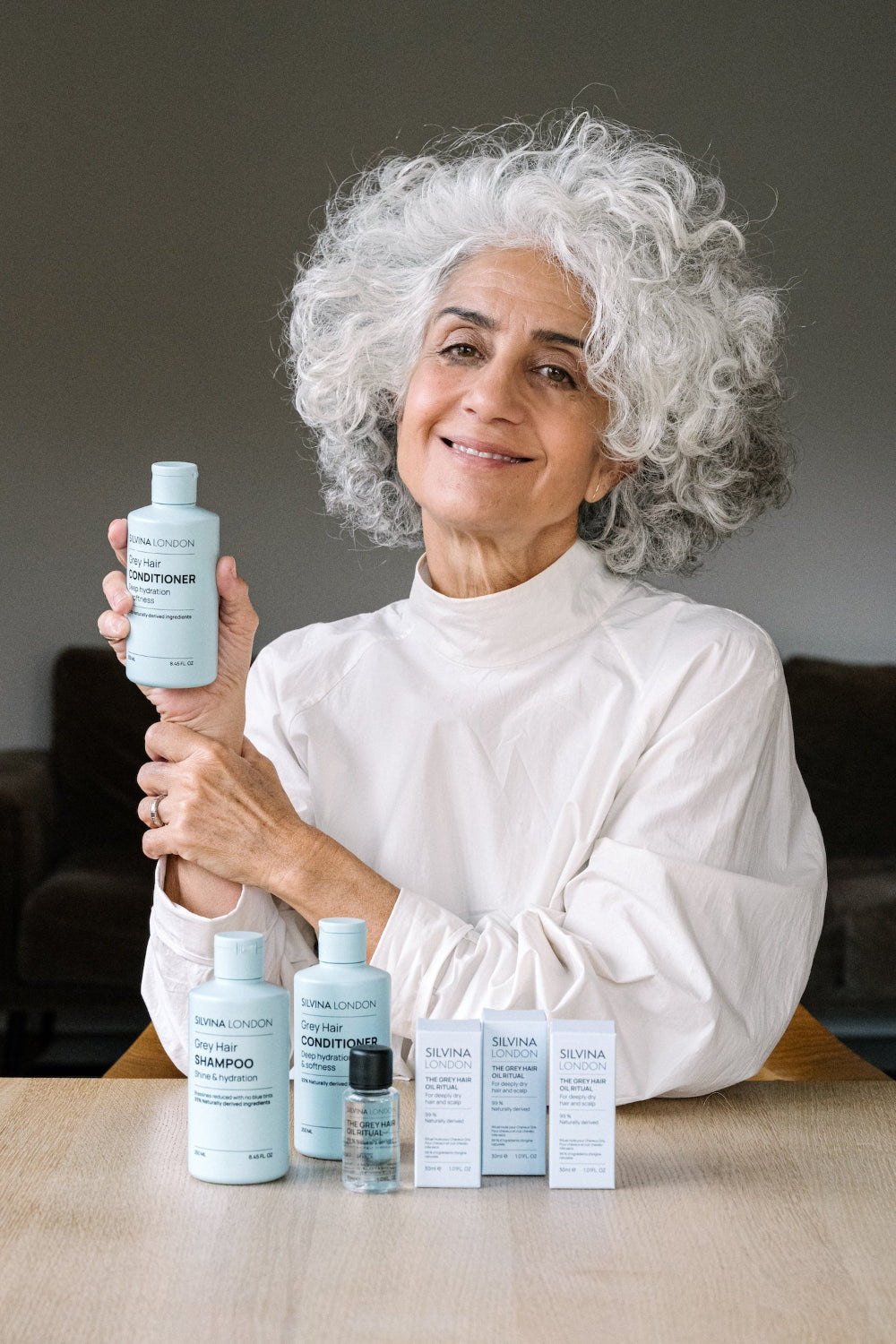 Woman holding a bottle of shampoo with various hair care products on a table