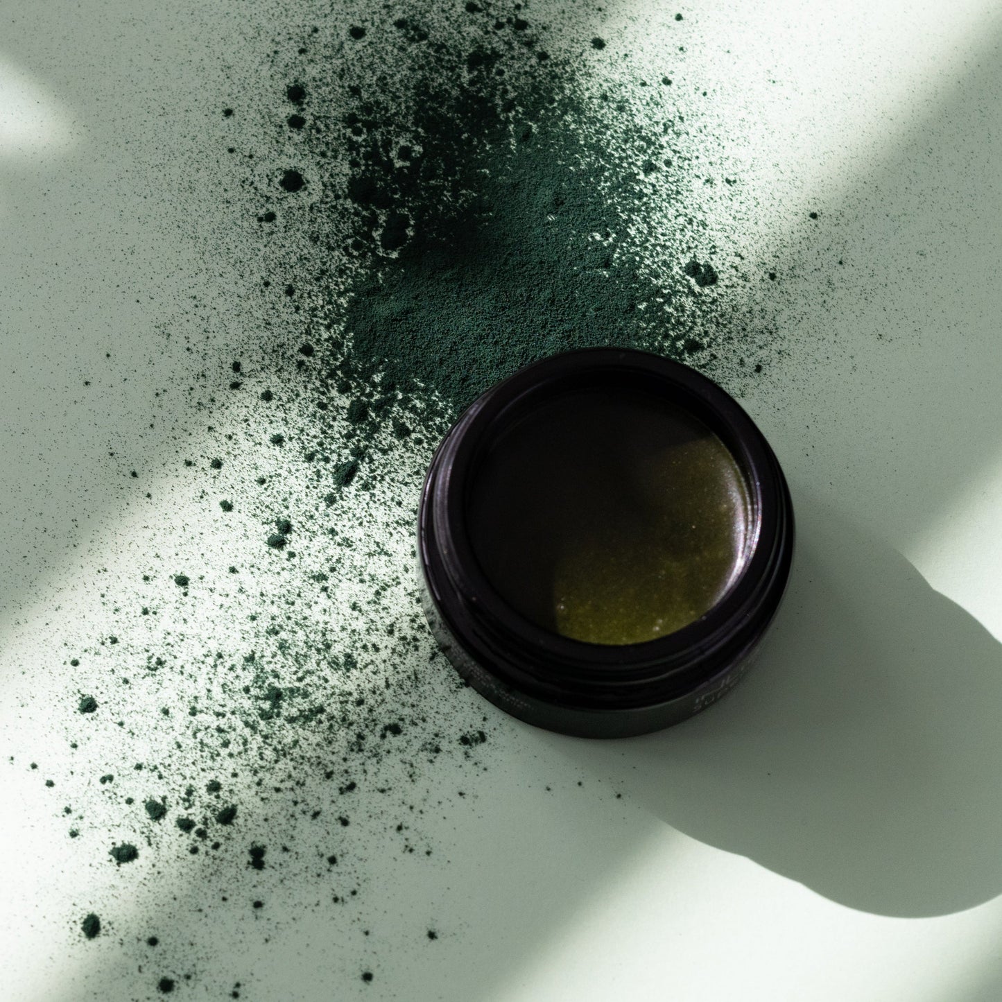 Open jar of Inlight Beauty Super-Food Mask 25ml with scattered powder on a white surface