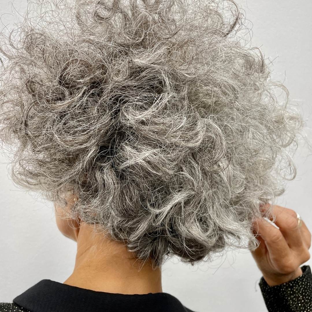 Close-up of a person with grey, curly hair against a plain background