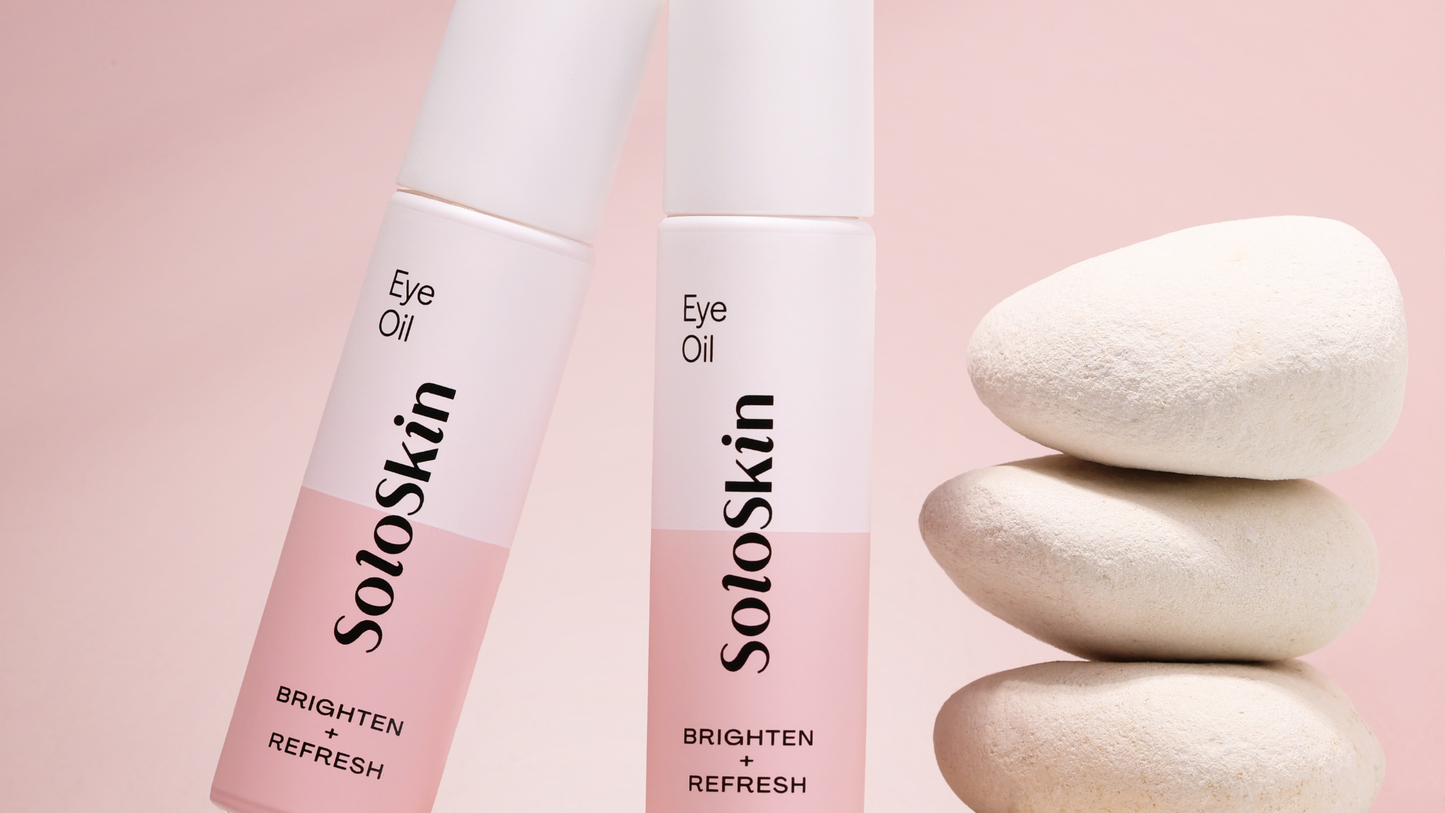 Two bottles of SoloSkin eye oil on a pink background with stones.
