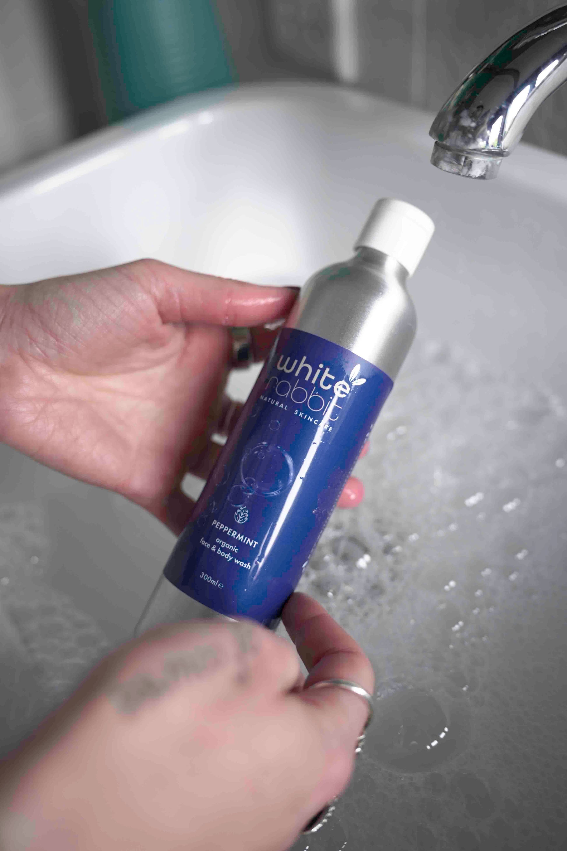 Hand holding a bottle labeled 'White Rabbit' over a sink with water running.