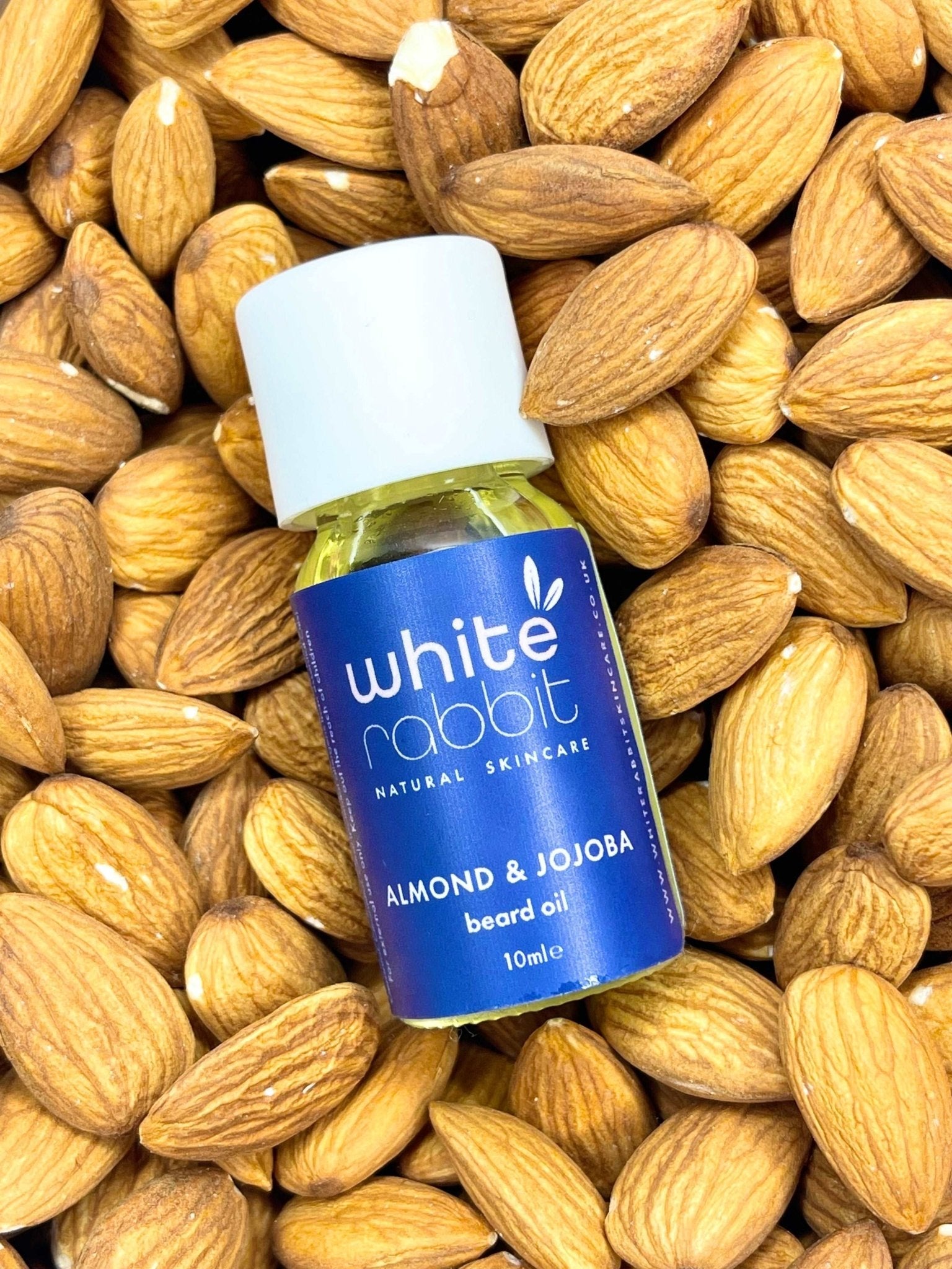 Bottle of White Rabbit almond and jojoba beard oil surrounded by almonds