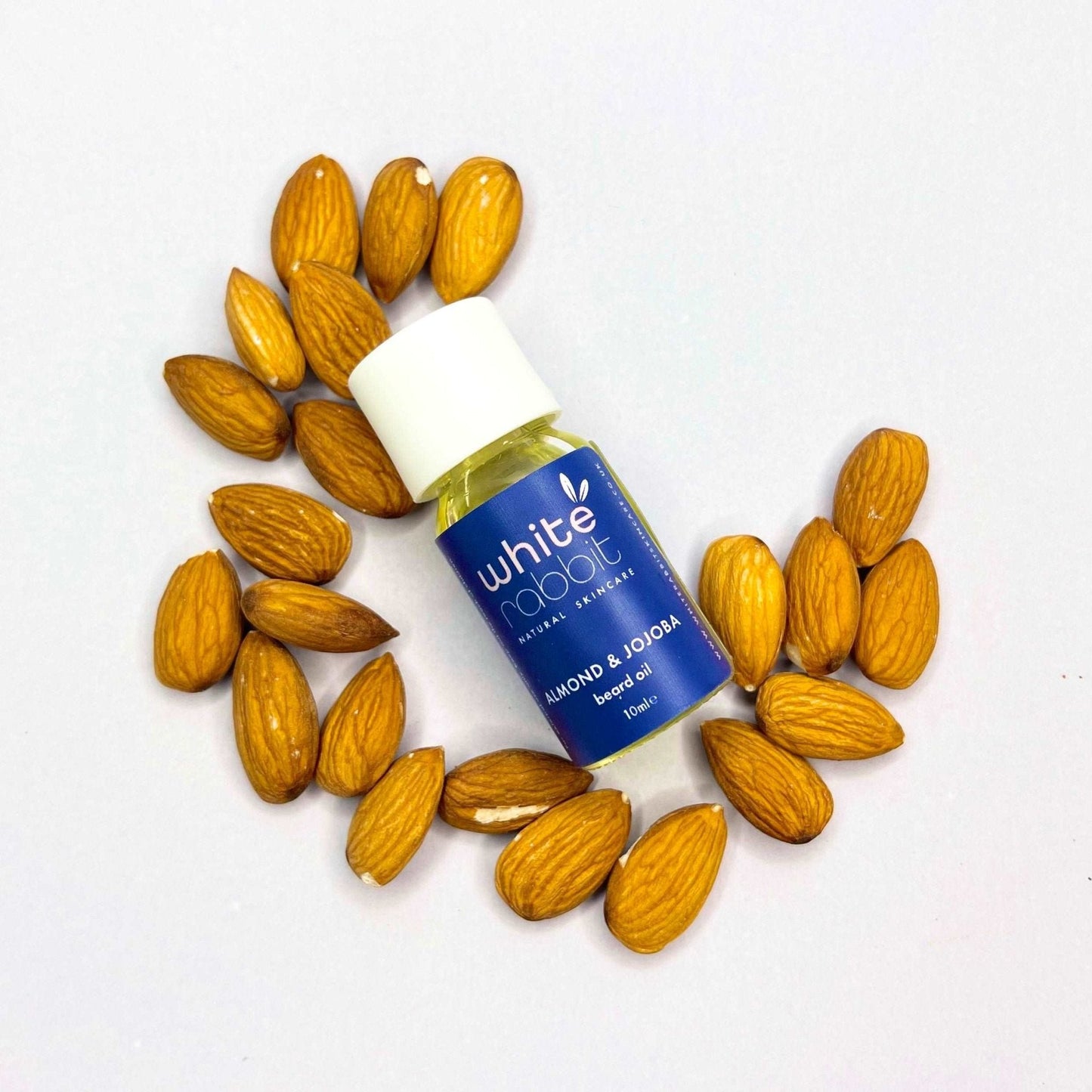Bottle of White Rabbit almond and jojoba oil surrounded by almonds on a white background