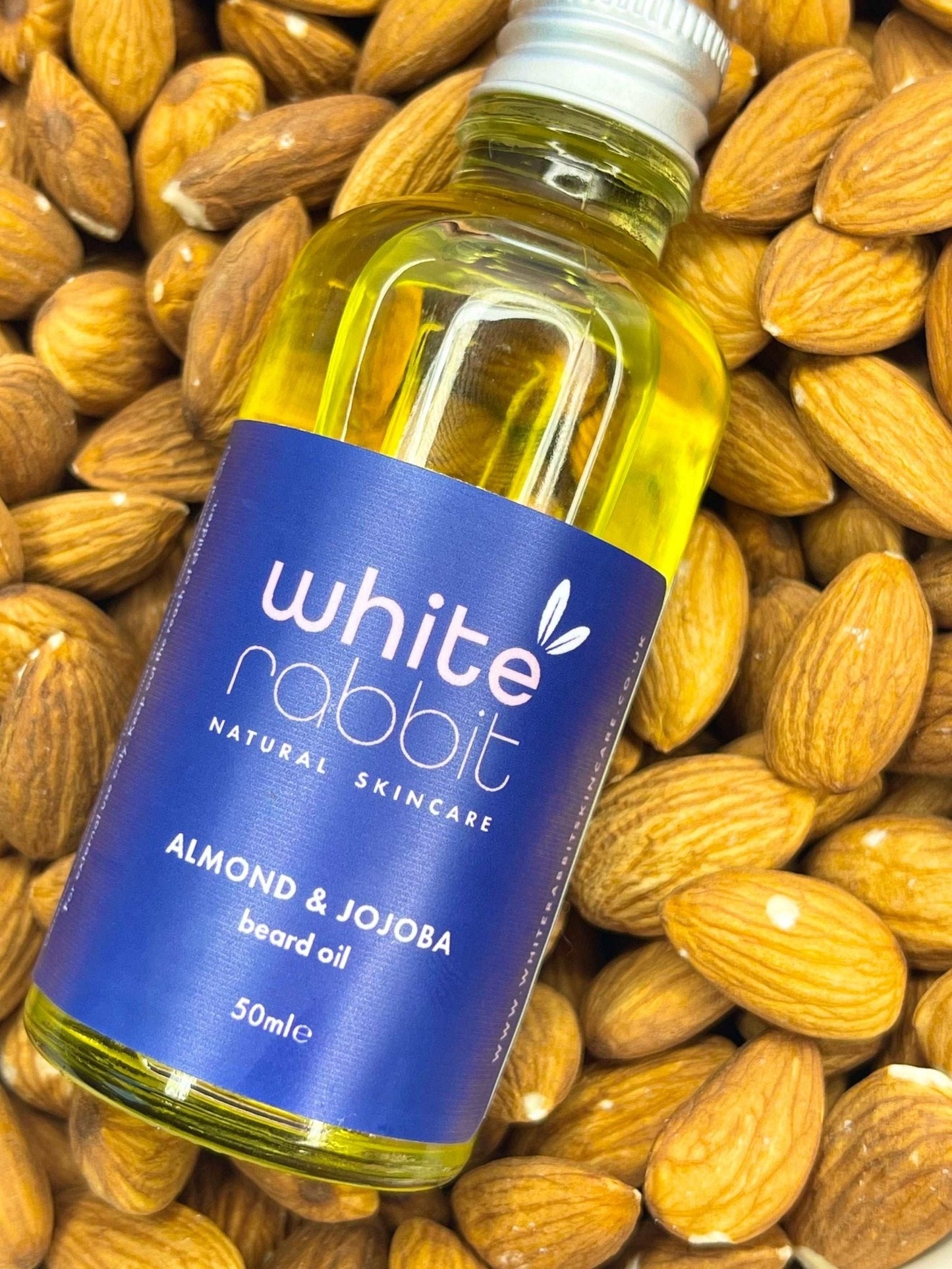 Bottle of White Rabbit Almond & Jojoba beard oil surrounded by almonds