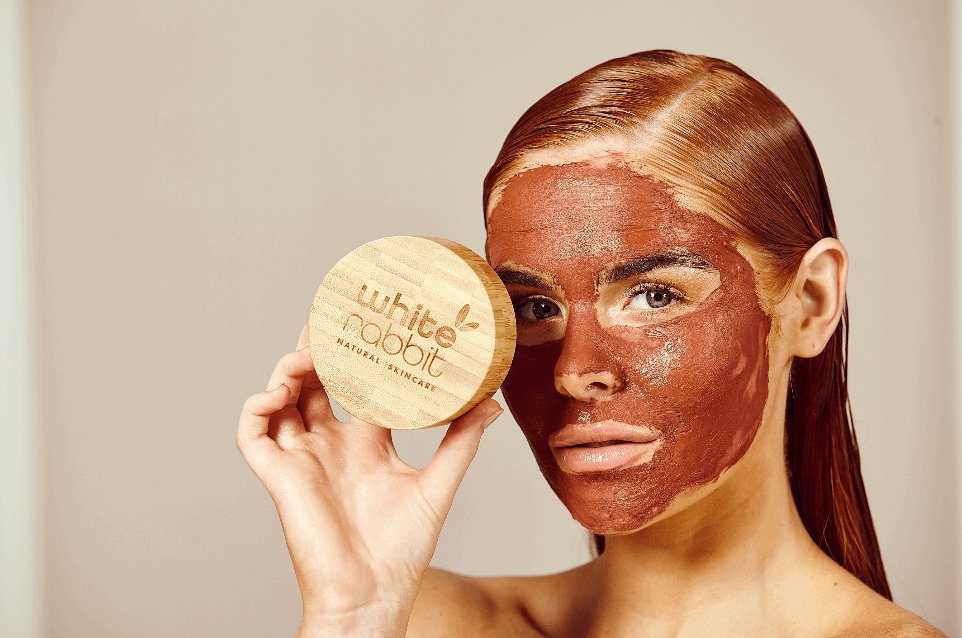Woman with a brown face mask holding a 'White Rabbit' product against a beige background